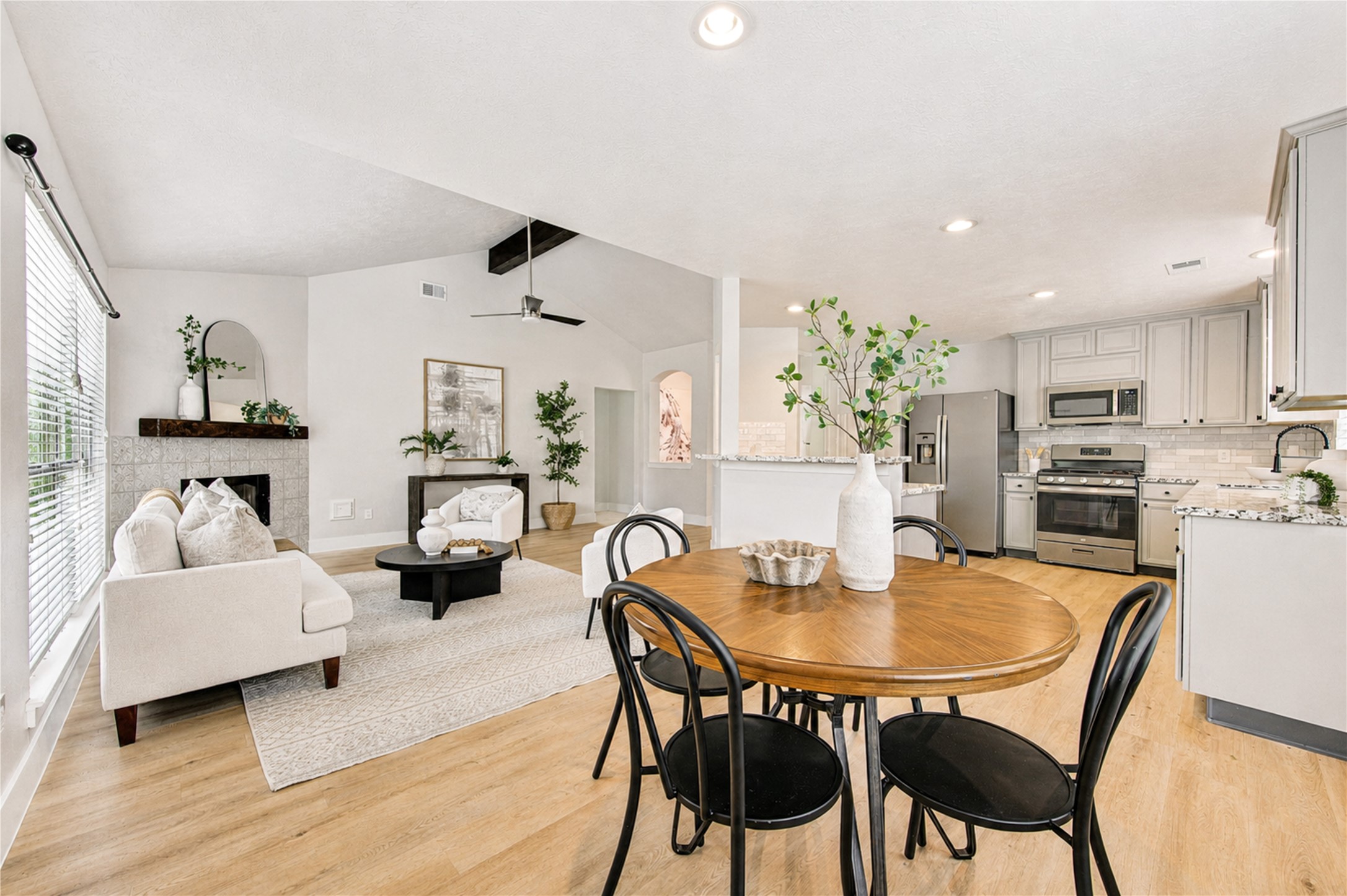 living room featuring a dramatic vaulted ceiling, rich wood beam, statement fireplace and polished sightlines into the kitchen