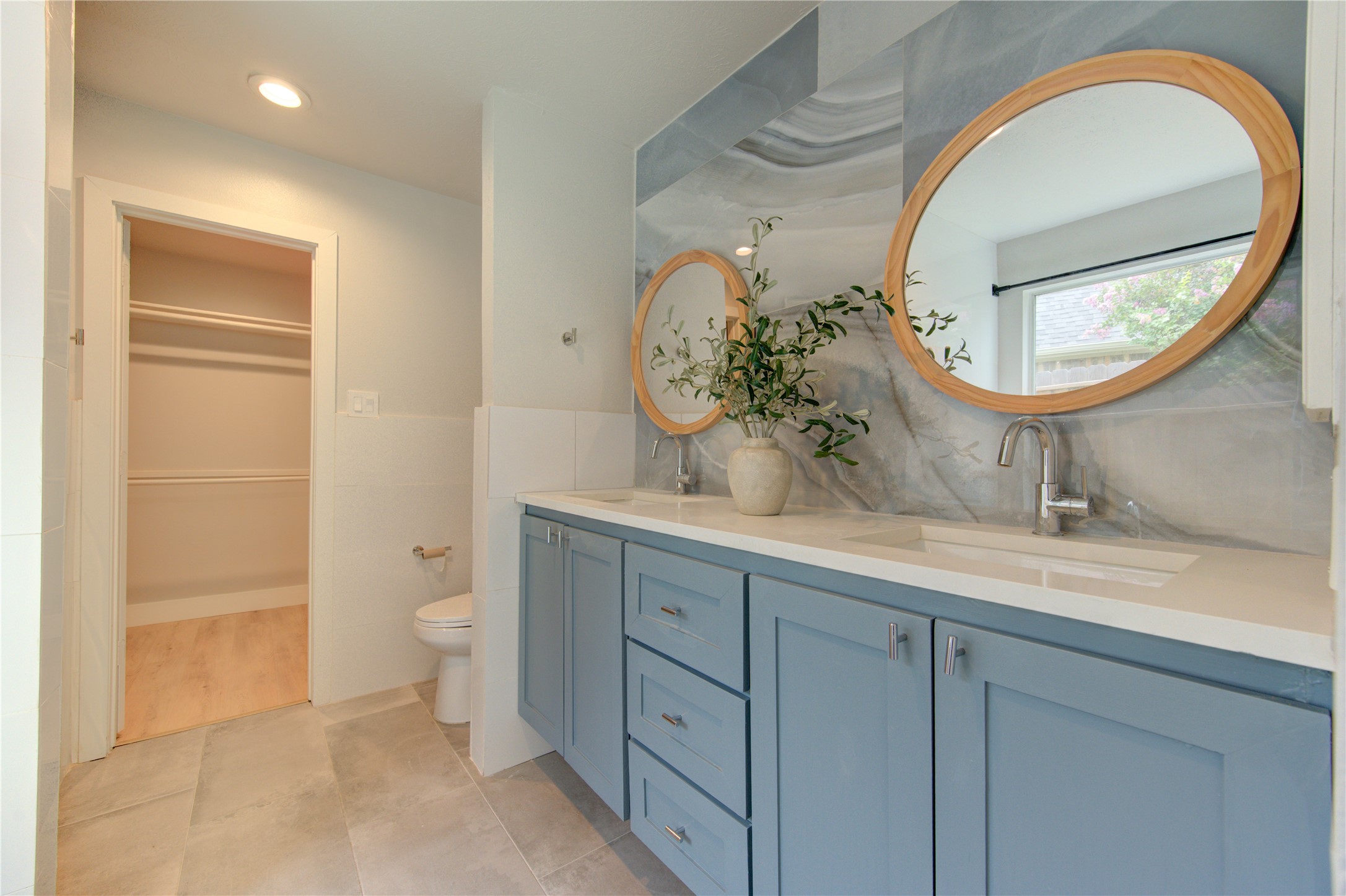 Stylish dual vanities with quartz countertops, modern cabinetry, round framed mirrors and striking designer tile create a luxurious everyday experience