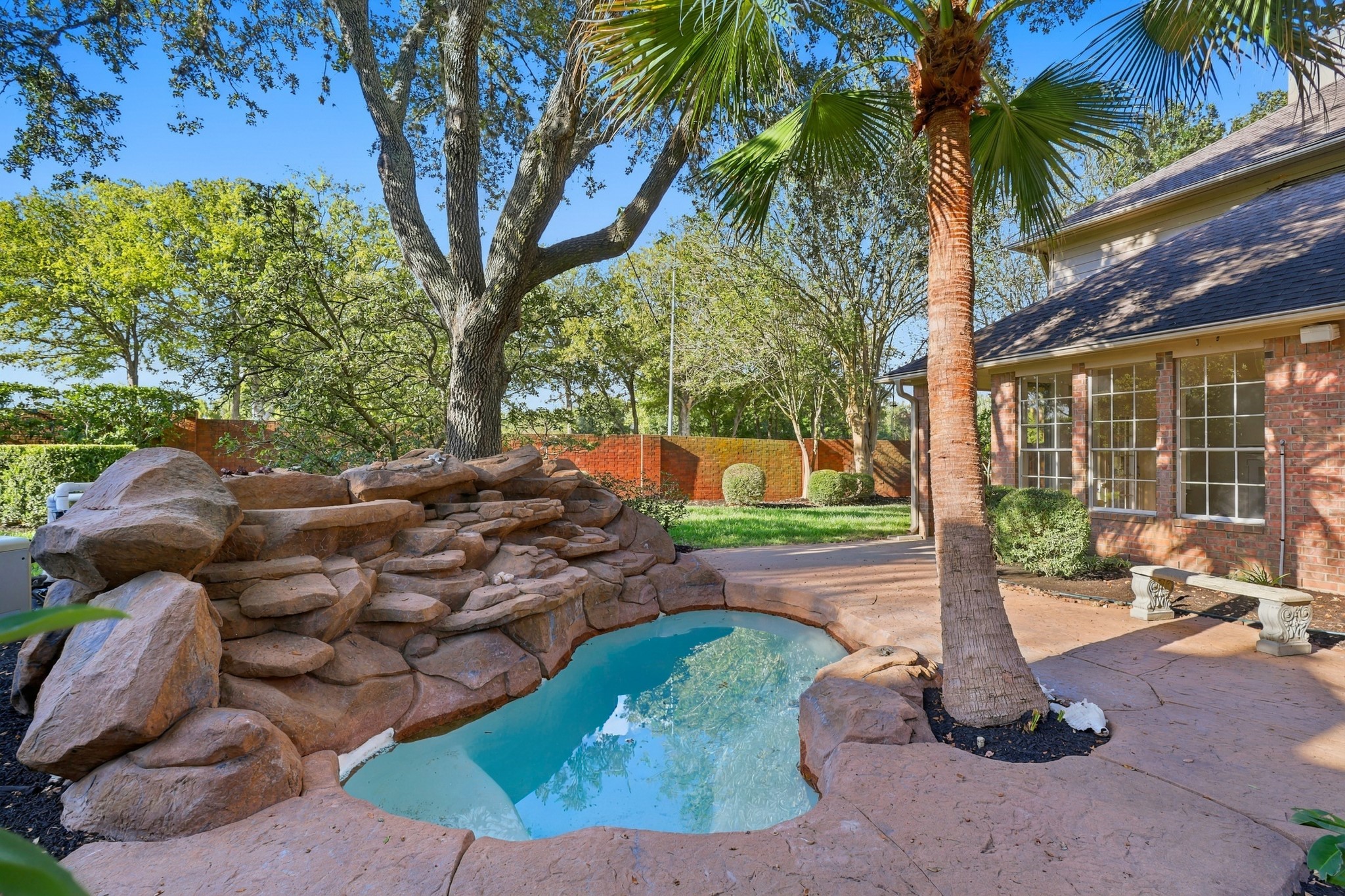 Charming backyard oasis featuring a natural rock waterfall cascading into a serene pool, surrounded by lush landscaping and mature trees for ultimate privacy and relaxation.