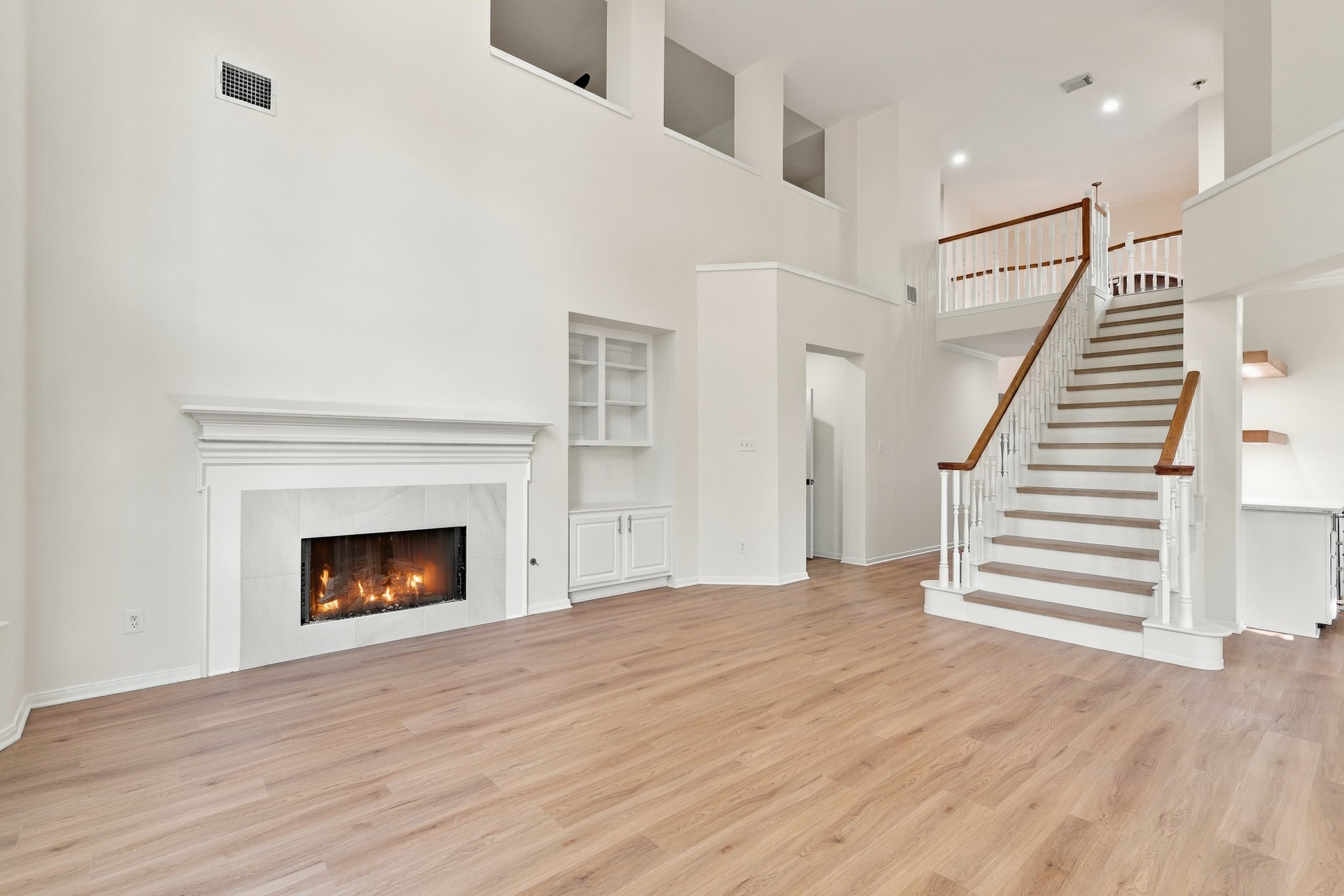 Spacious living area featuring a cozy fireplace, elegant staircase, and open layout with abundant natural light.