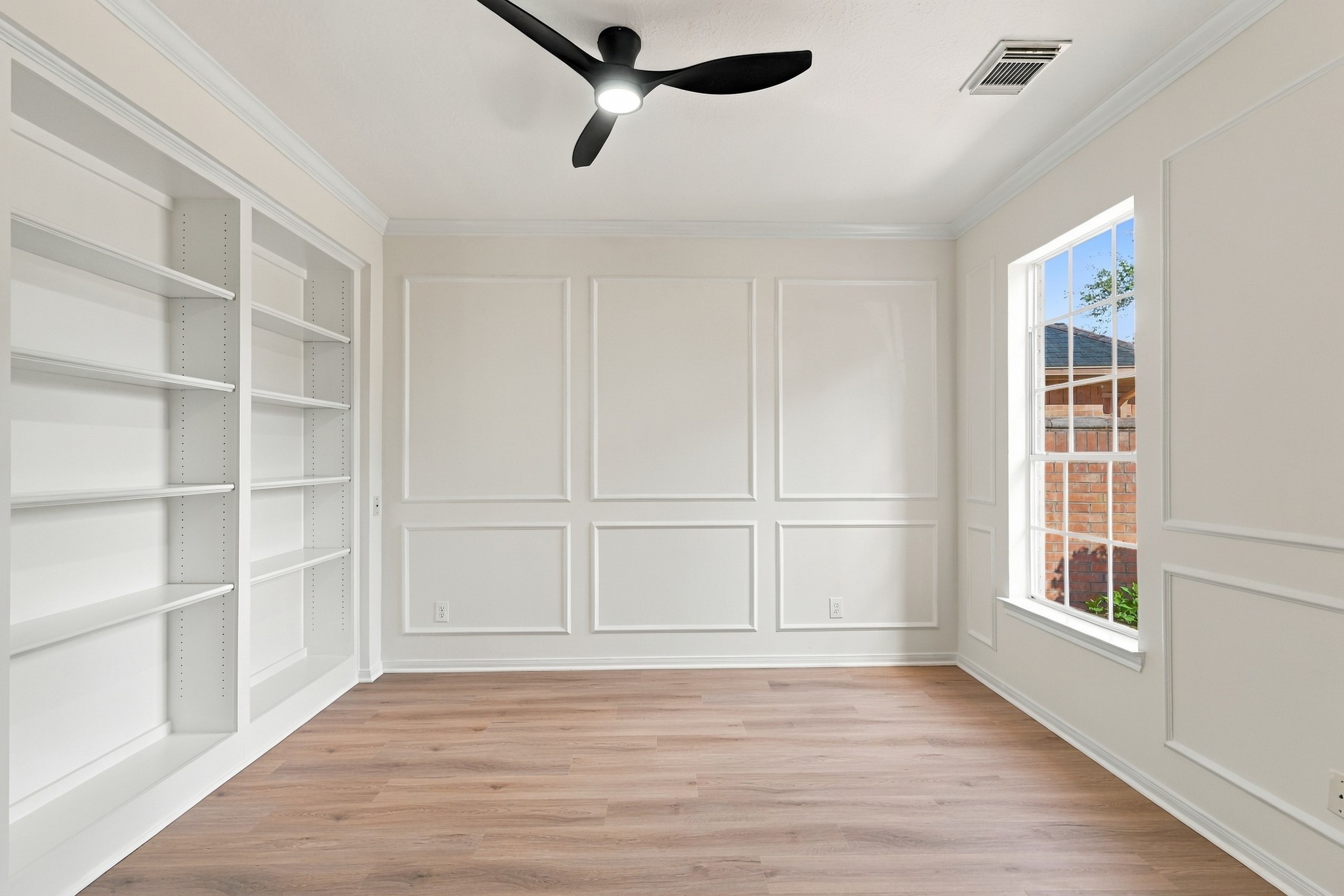 Bright and inviting room with elegant wainscoting, built-in shelving, and a large window offering abundant natural light.