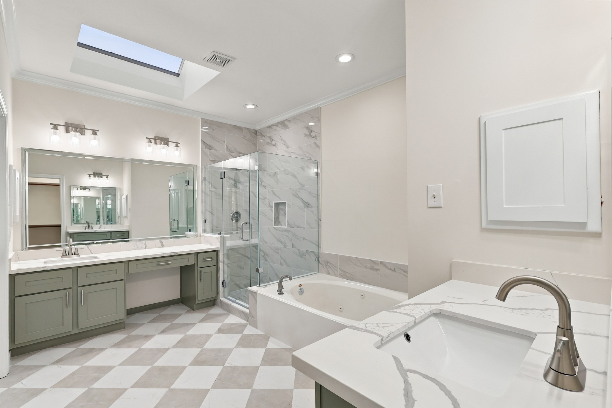 Spacious and elegant bathroom featuring a luxurious soaking tub, glass-enclosed shower, dual vanities with ample counter space, and a skylight for natural lighting.