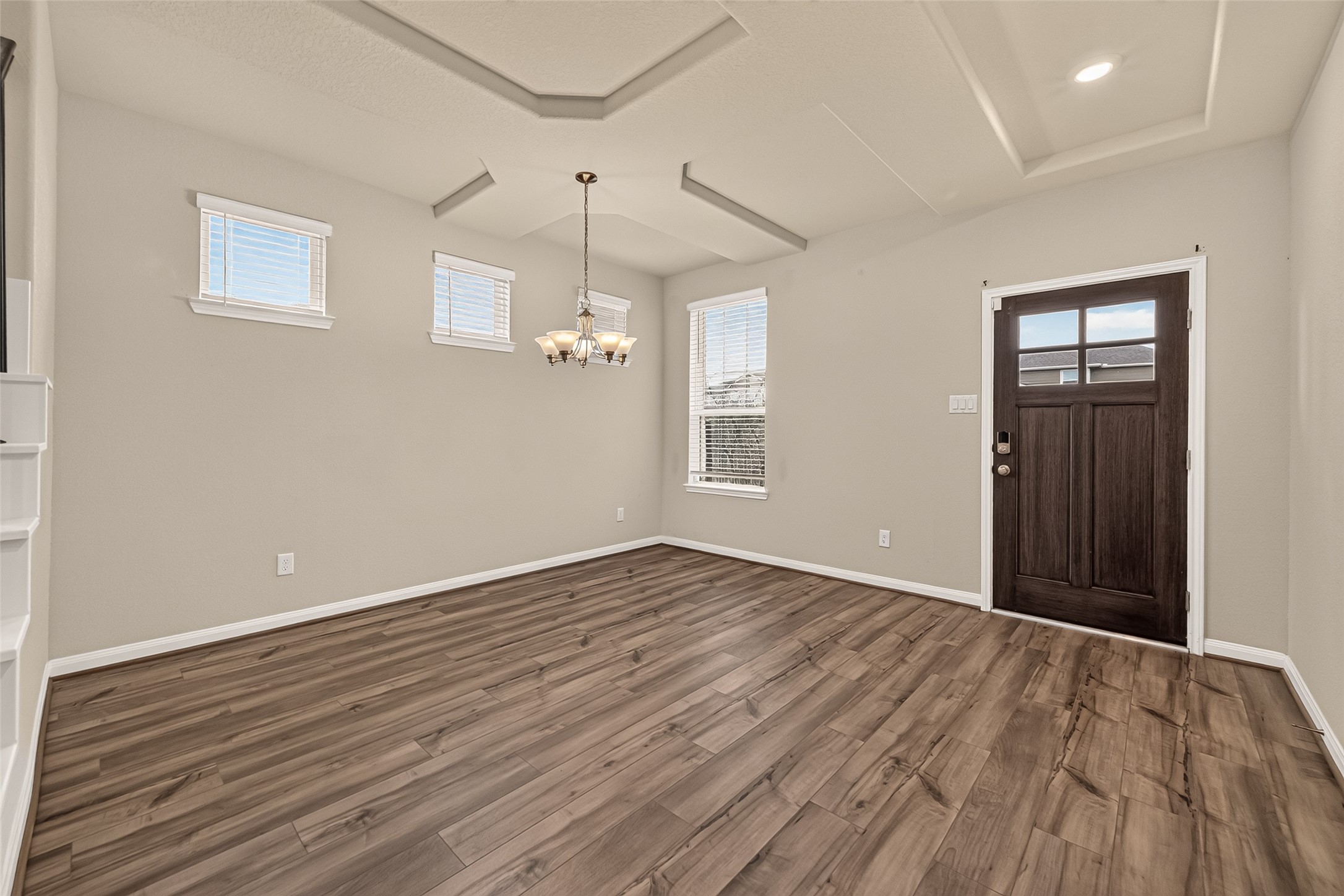 Elegant entryway featuring a stylish chandelier and ample natural light from multiple windows, complemented by a dark wood front door.