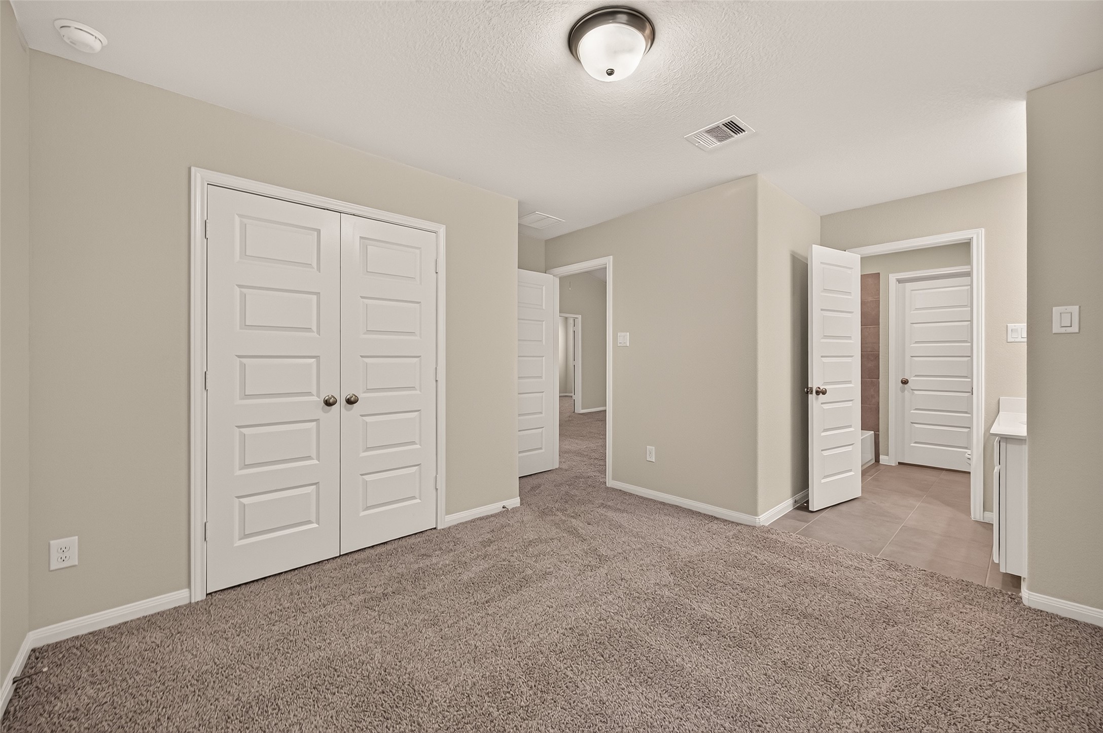 Spacious secondary bedroom with jack and jill bathroom access. Plush carpet, neutral walls, and ample closet space, featuring elegant white doors and a cozy, inviting atmosphere.