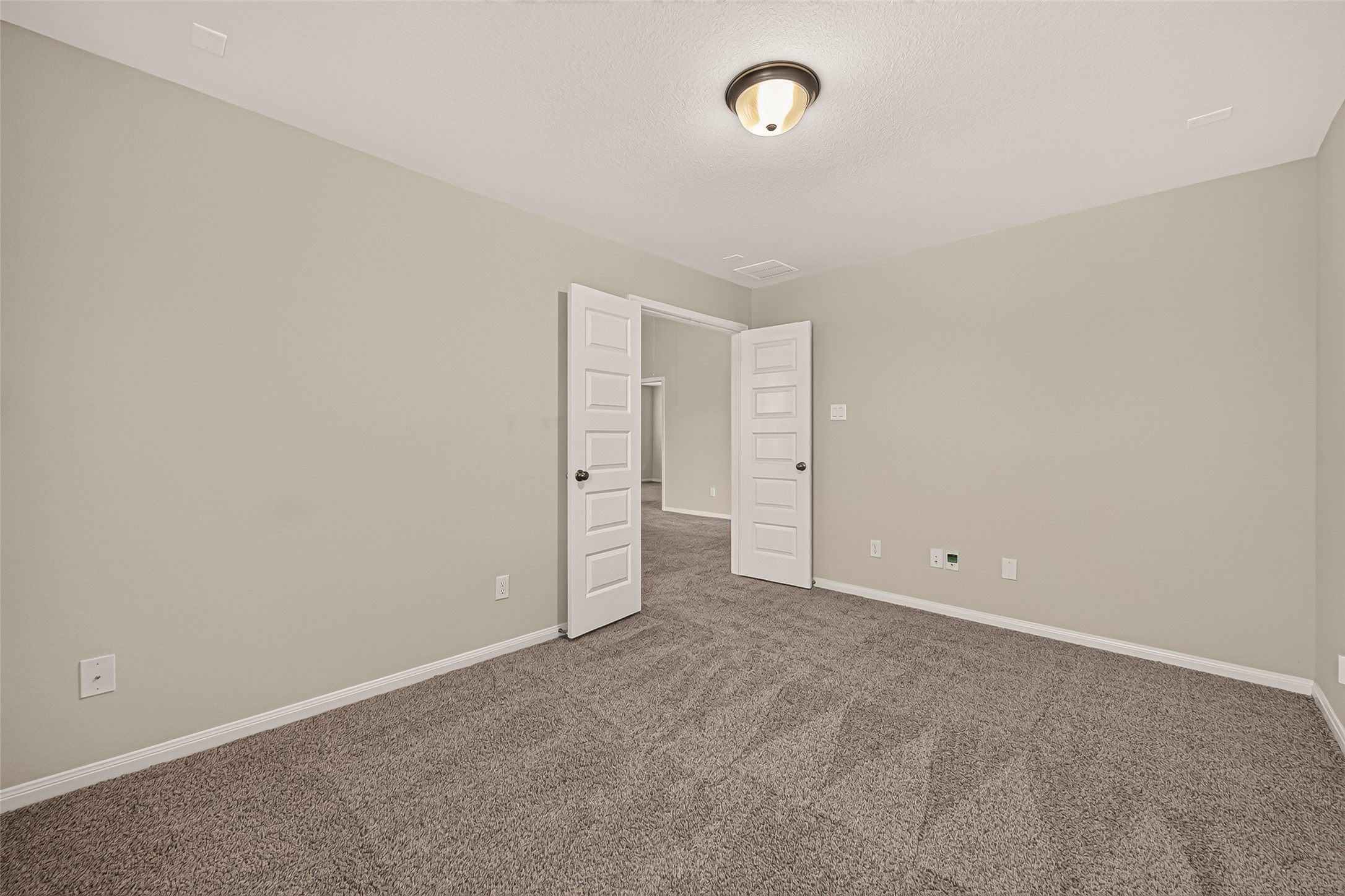 Spacious media room or flex space with plush carpet, neutral walls, and ample natural light, featuring modern fixtures and an open doorway for seamless flow.