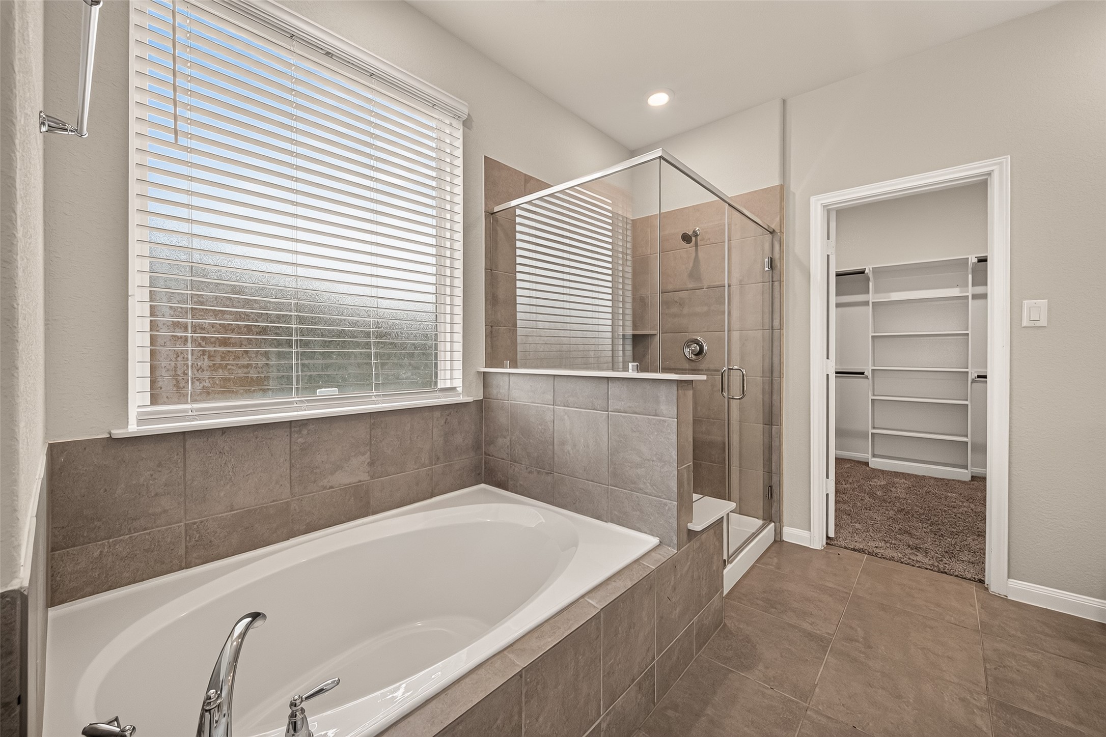 Luxurious bathroom featuring a spacious soaking tub and a sleek glass-enclosed shower, complemented by a walk-in closet for ample storage.