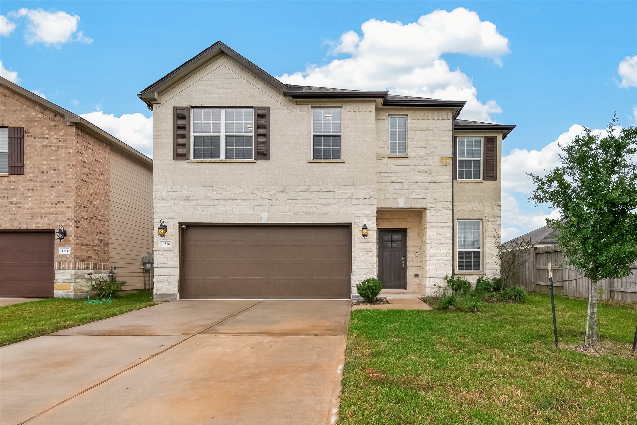 Charming two-story home with a modern stone faade, featuring a spacious double garage and a nicely maintained front lawn.