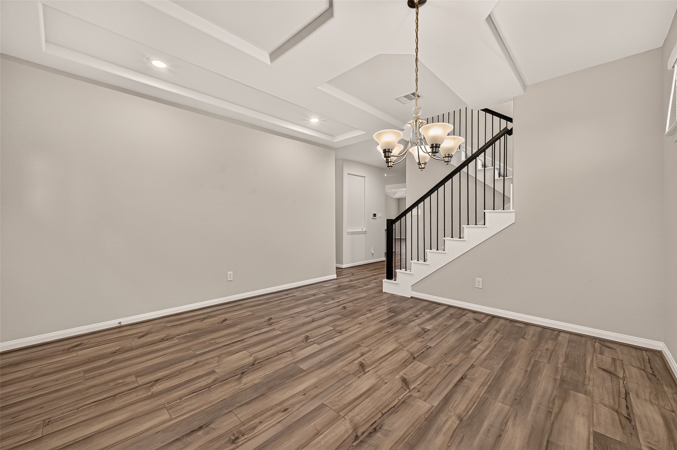 Elegant dining area features a sleek staircase with modern railings, accented by a coffered ceiling with recessed lighting.