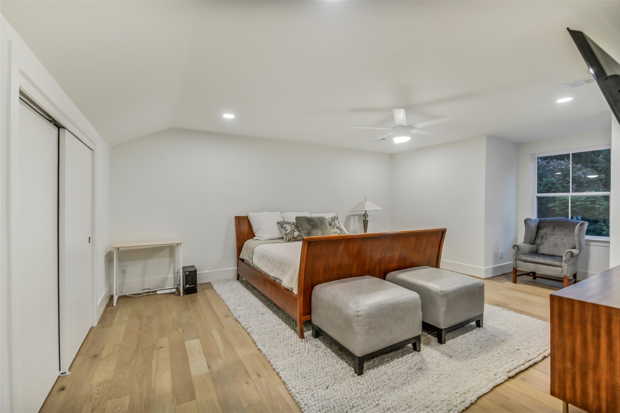 A spacious upstairs bedroom with vaulted ceilings, a large closet, and a bright window seating area. Light wood flooring and generous proportions offer plenty of room for both sleeping and lounging space.