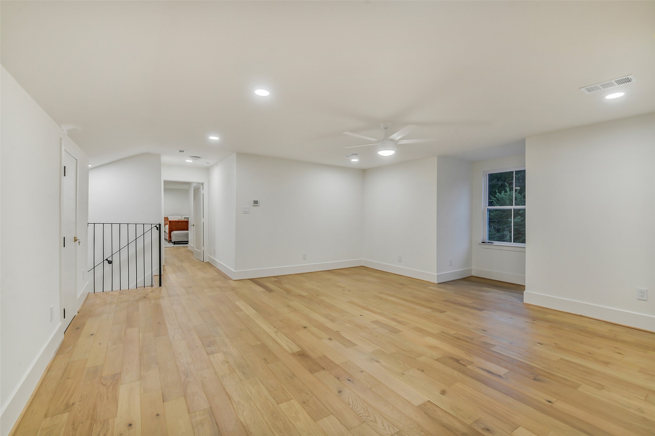 A spacious upstairs living area, ideal as a game room, media space, or additional lounge. Wood flooring, a ceiling fan, and a bright window keep the space light-filled, with easy access to the bedrooms and staircase down to the main level.