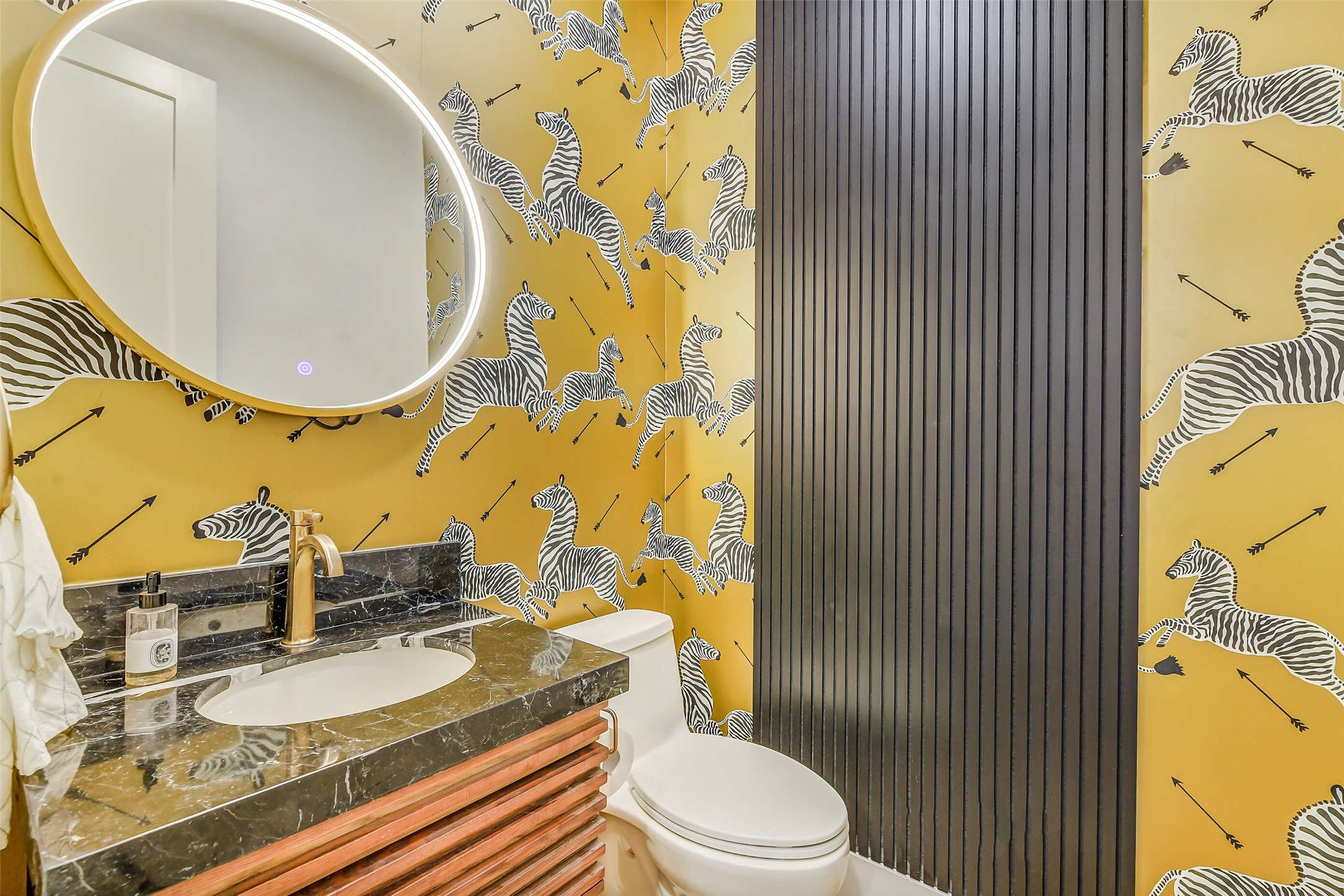 Vibrant, hand-painted-style wallpaper in warm golden hues makes a statement in this powder bath, paired with a sleek floating vanity, oval mirror, and warm brass fixtures for a stylish finish.
