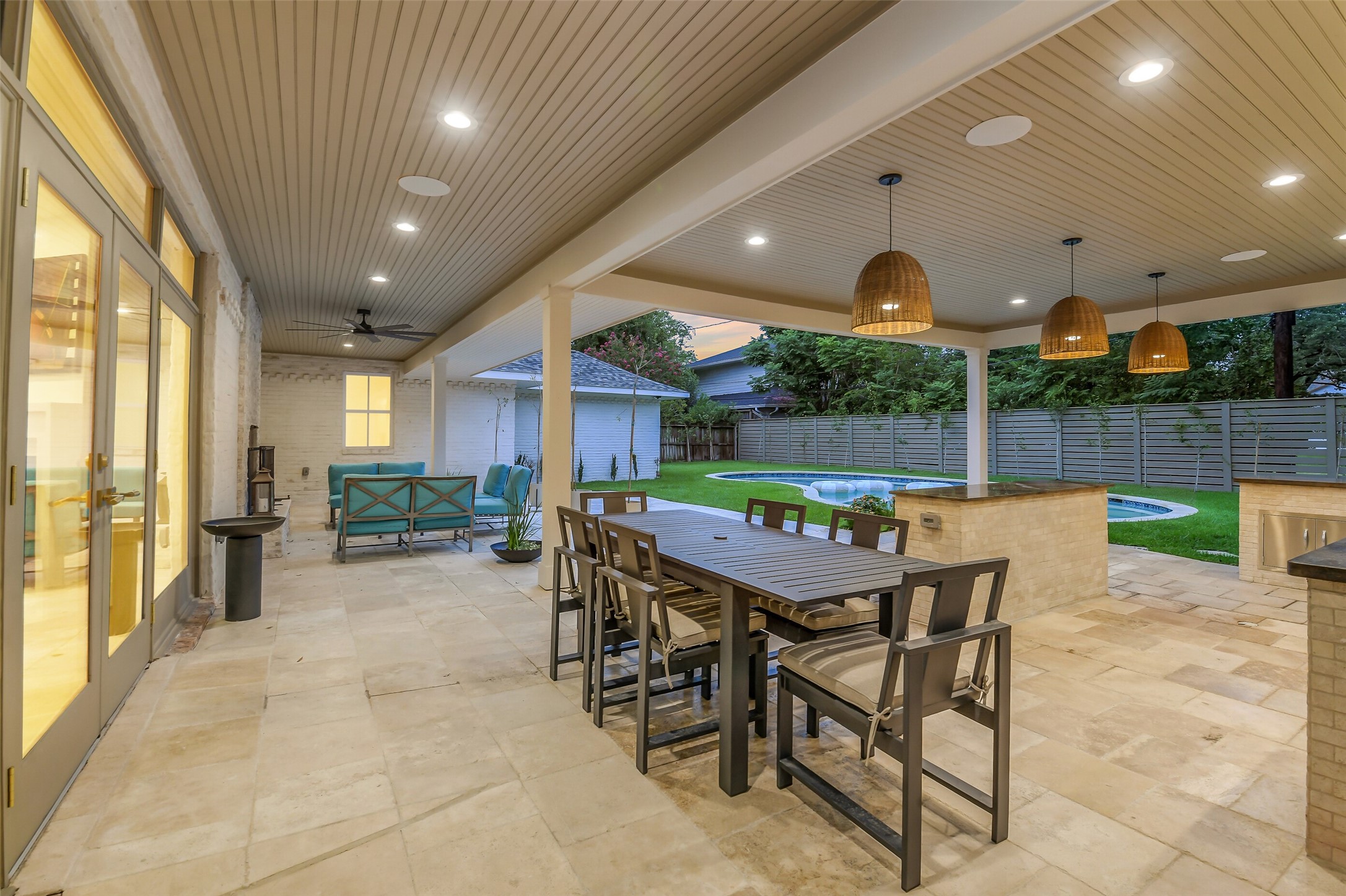 A resort-style covered patio featuring a full outdoor kitchen with bar seating, a wood-look ceiling with recessed lighting, and a dining area overlooking the pool  perfect for year-round entertaining and al fresco dining.