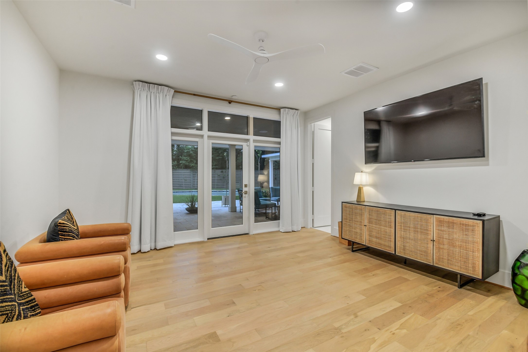 A bright, versatile bedroom with French doors opening directly onto the backyard and pool, offering seamless indoor-outdoor access. Light wood flooring, a ceiling fan, and generous space complete this comfortable retreat.