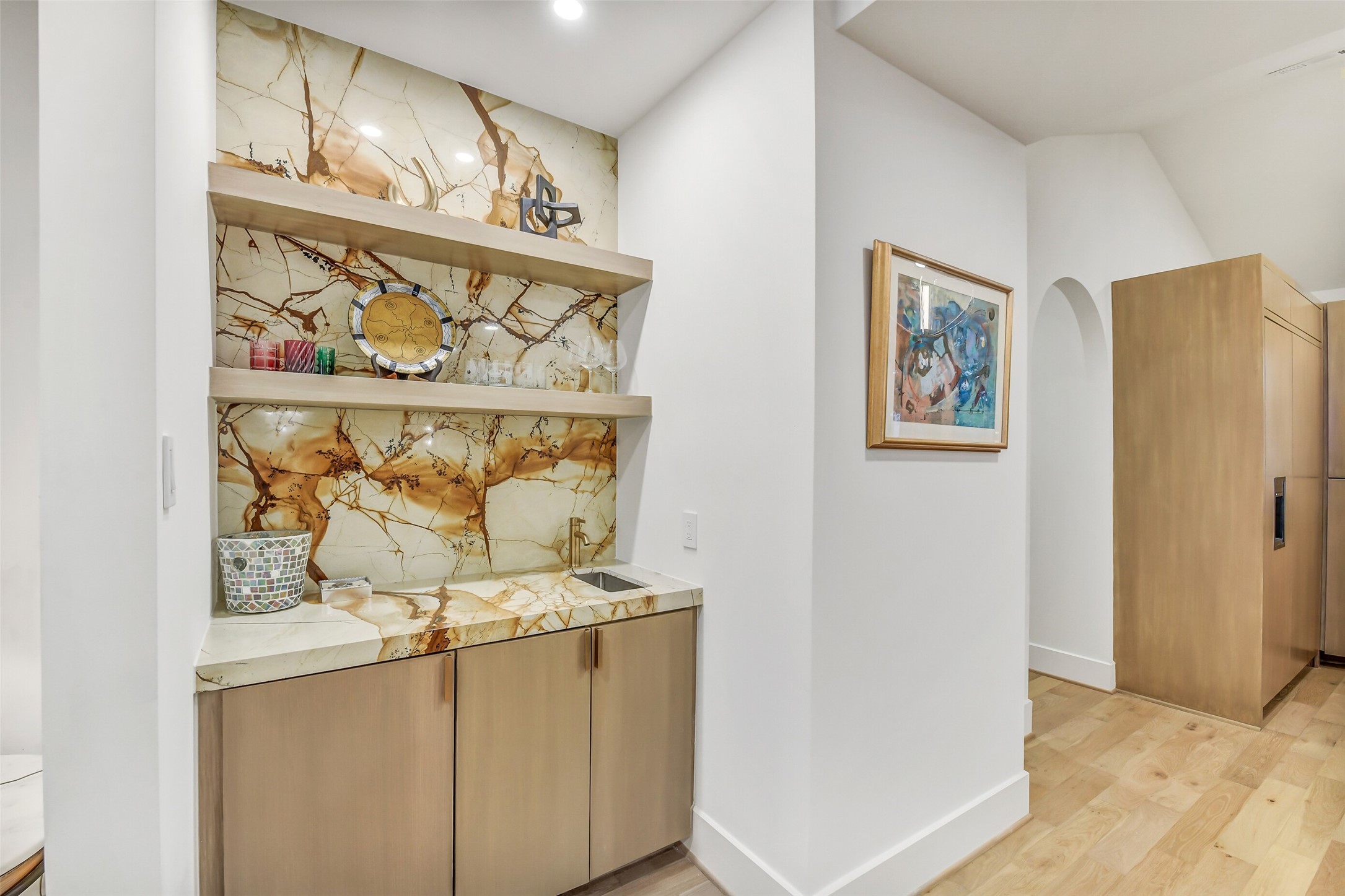 A stylish wet bar tucked just off the main living space, featuring dramatic natural stone backsplash, open shelving, and warm wood cabinetry  perfect for storing glassware and entertaining essentials.
