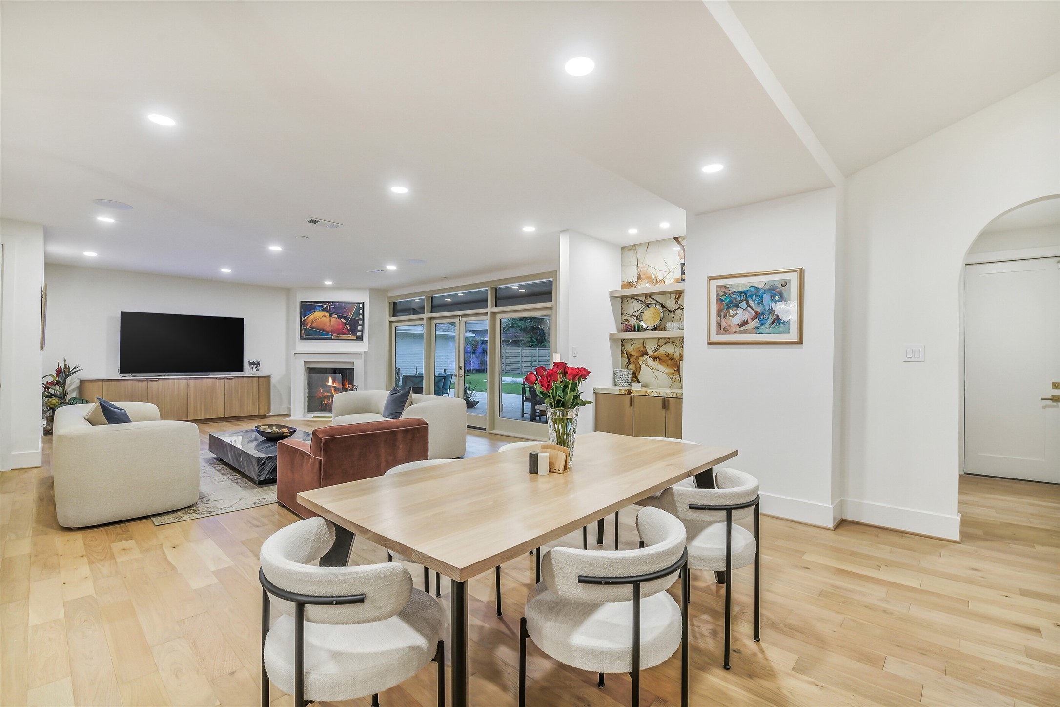 A relaxed gathering space with a built-in console, layered seating, and a large shared ottoman perfect for movie nights or casual hangouts. Curved built-ins and an arched entryway add character, while soft neutral tones and light wood floors keep the room bright and airy.