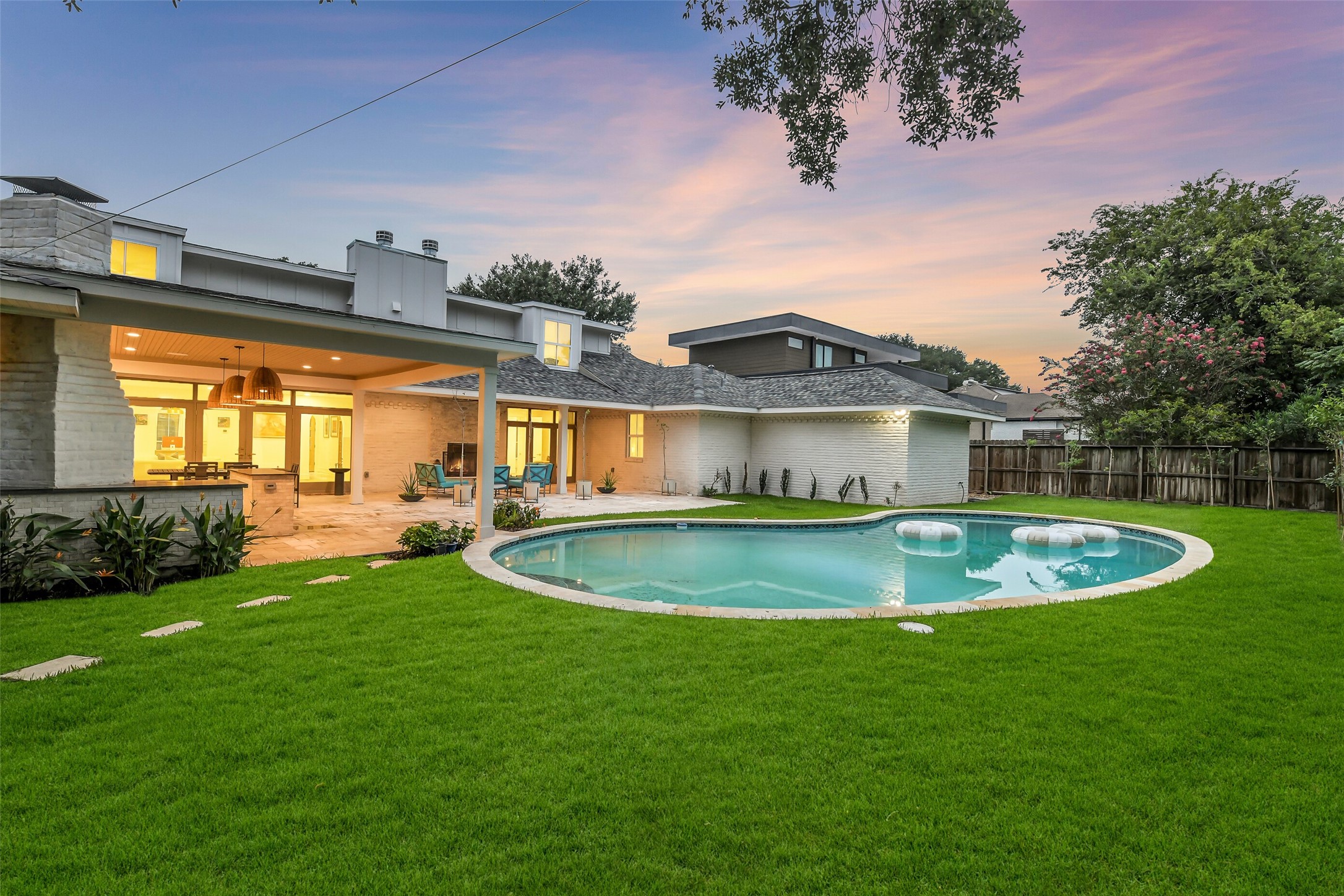 Sleek modern exterior, sparkling pool, and expansive lawn. Mature trees provide privacy on all sides, framing this beautifully designed outdoor retreat.