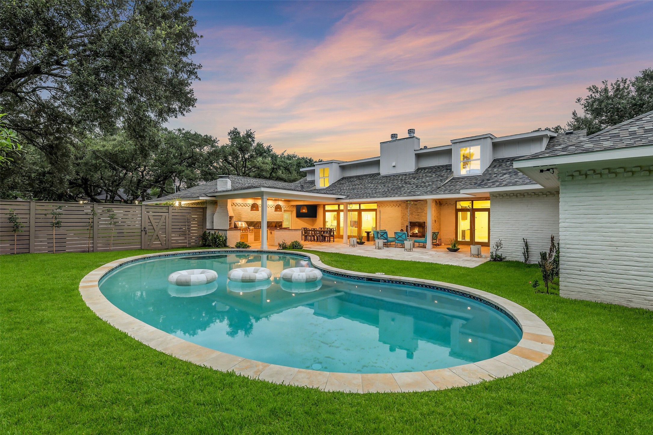 A freeform pool anchors this beautifully landscaped backyard, surrounded by lush green lawn and mature trees for privacy. The adjoining covered patio adds an outdoor kitchen and fireplace, creating a seamless indoor-outdoor flow  an entertainer's paradise from morning through dusk.