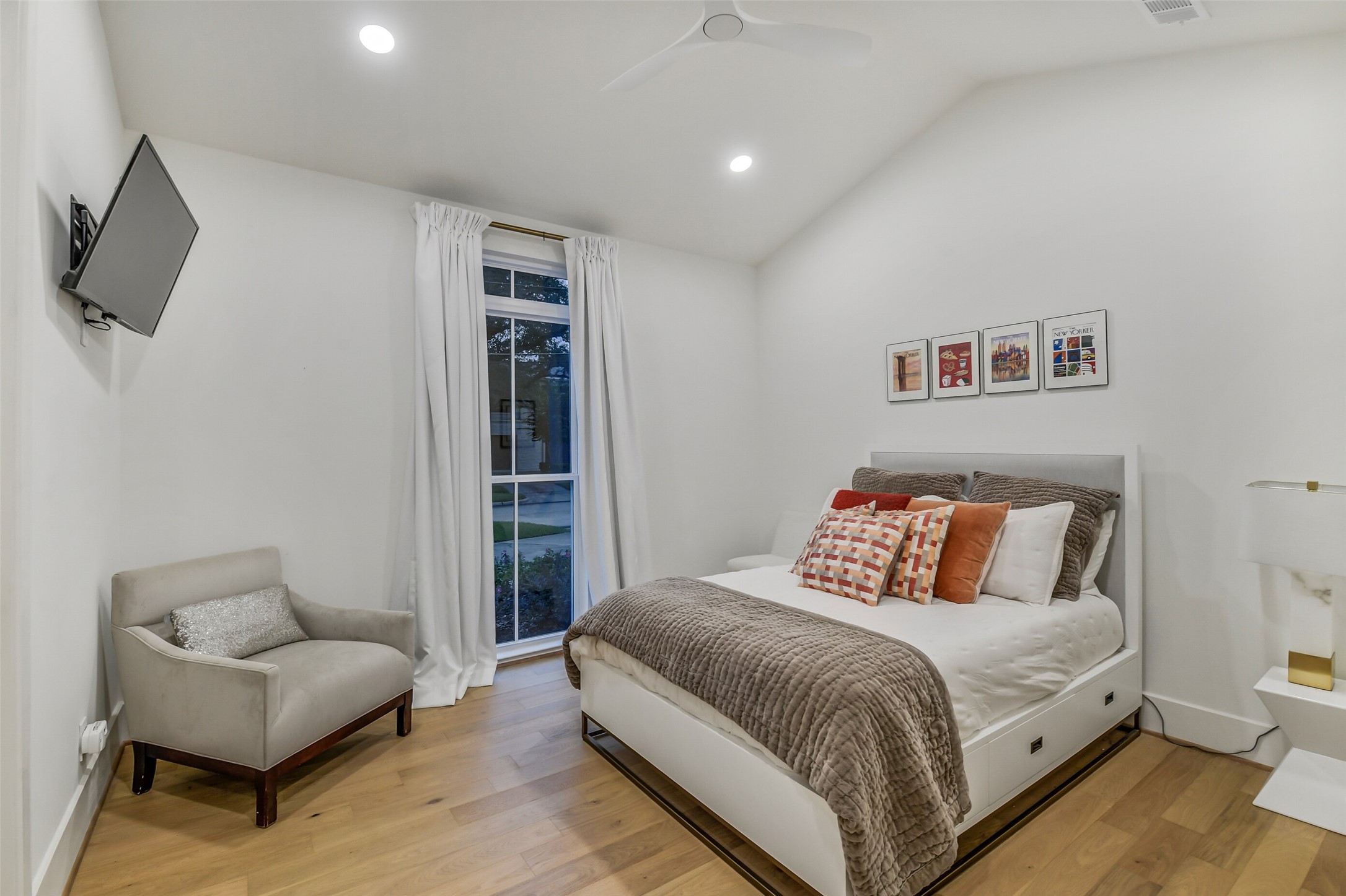 A bright, comfortable bedroom featuring a vaulted ceiling and a large window with natural light  each secondary bedroom offers its own distinct ceiling design, adding character throughout the home.
