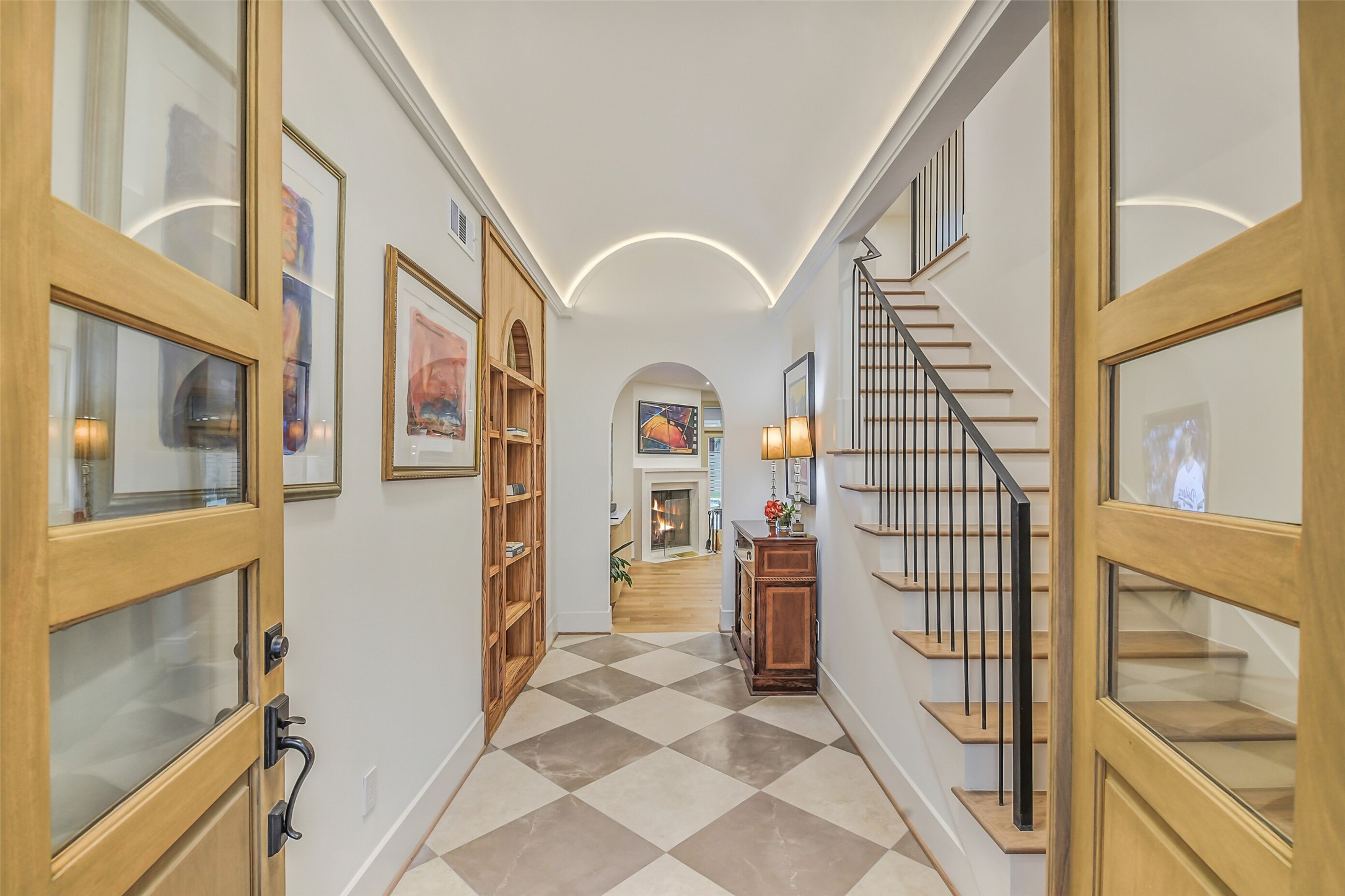 Step through elegant double doors into a stunning foyer featuring cove lit barrel ceilings, a dramatic staircase, and beautiful stone tile flooring.