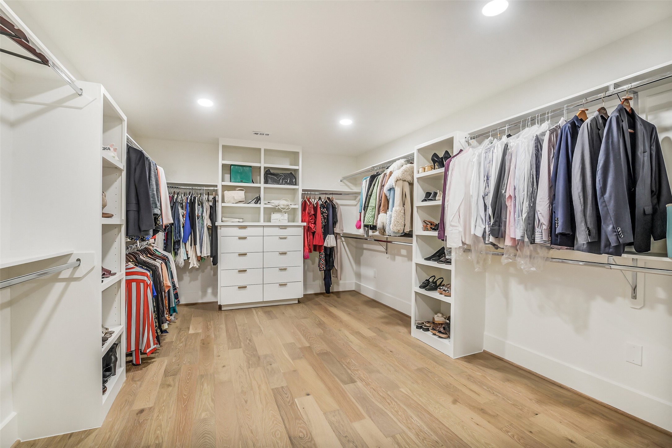 A massive walk-in closet outfitted with custom built-ins, ample hanging space, and a center island of drawers for organized storage. Shoe shelving, open cubbies, and a spacious layout make this a true dream closet.