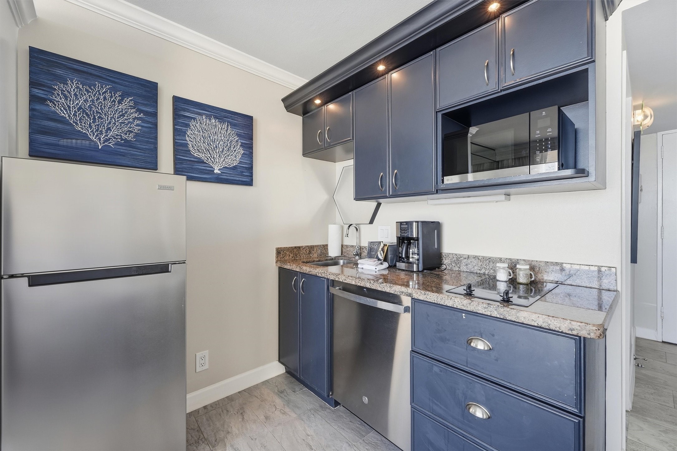 The kitchenette features navy cabinetry, a stainless steel refrigerator, microwave, and dishwasher.