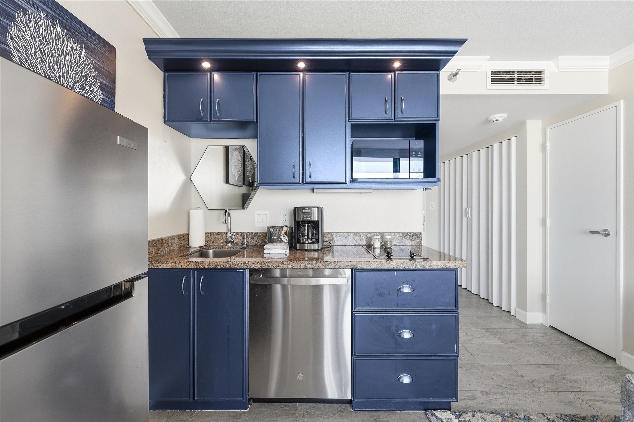 Coordinating countertops, cabinet lighting, and a mirrored backsplash complement the coastal blue cabinetry.