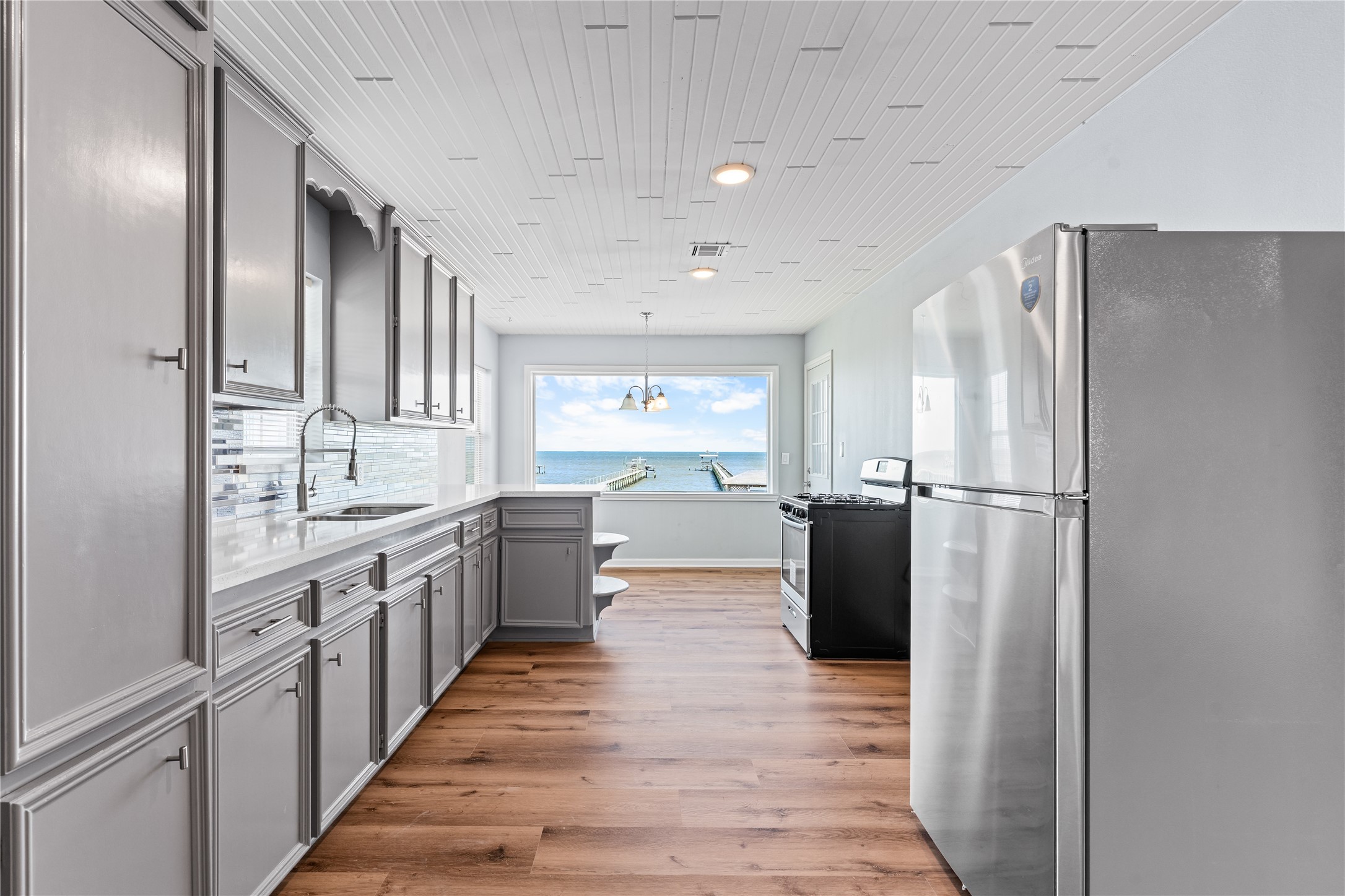 The eye naturally moves from tailored cabinetry and quartz surfaces to the expansive bay beyond, creating a kitchen that feels both grounded and effortlessly connected to its surroundings.