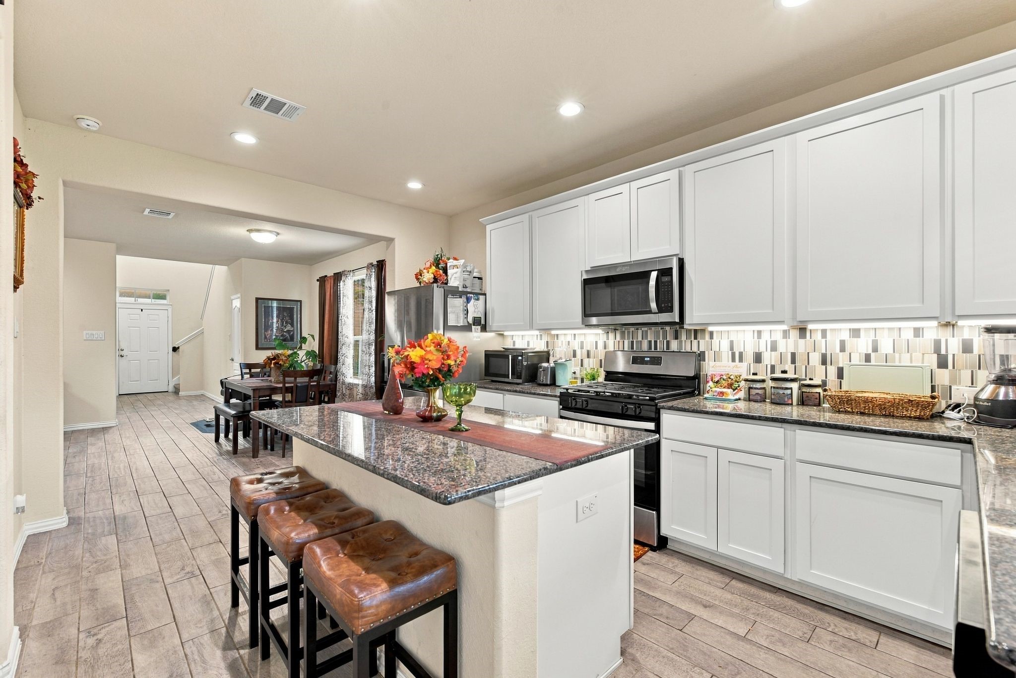 Beautiful and modern kitchen with sleek white cabinetry, granite countertops, and a stylish tile backsplash. An inviting breakfast bar with seating opens to a cozy dining area, perfect for family gatherings.