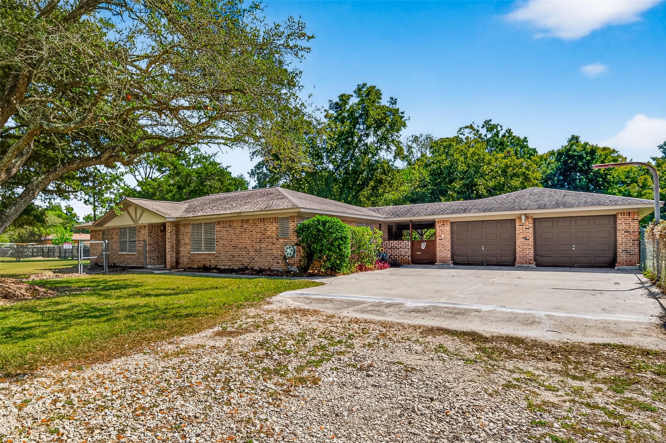 This is a spacious, single-story brick home with a three-car garage and a large driveway. The property features a well-maintained lawn with mature trees, offering a serene and private setting.