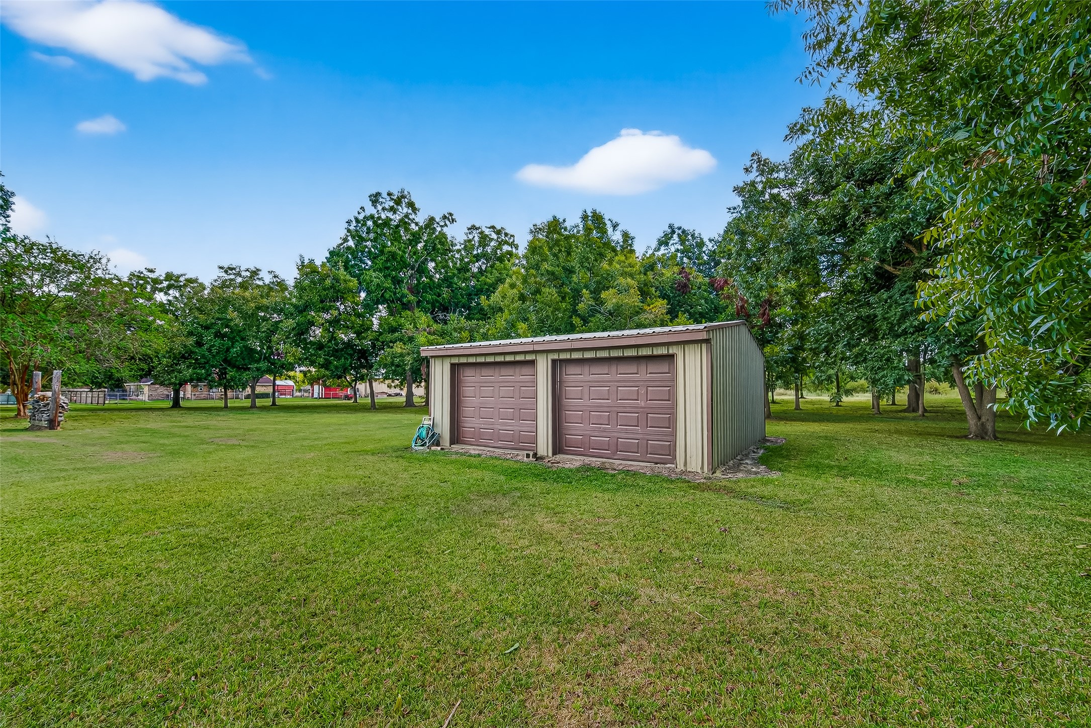 This photo shows a spacious backyard featuring a workshop for enthusiast or side business, surrounded by lush green grass and mature trees, providing a serene and private setting.