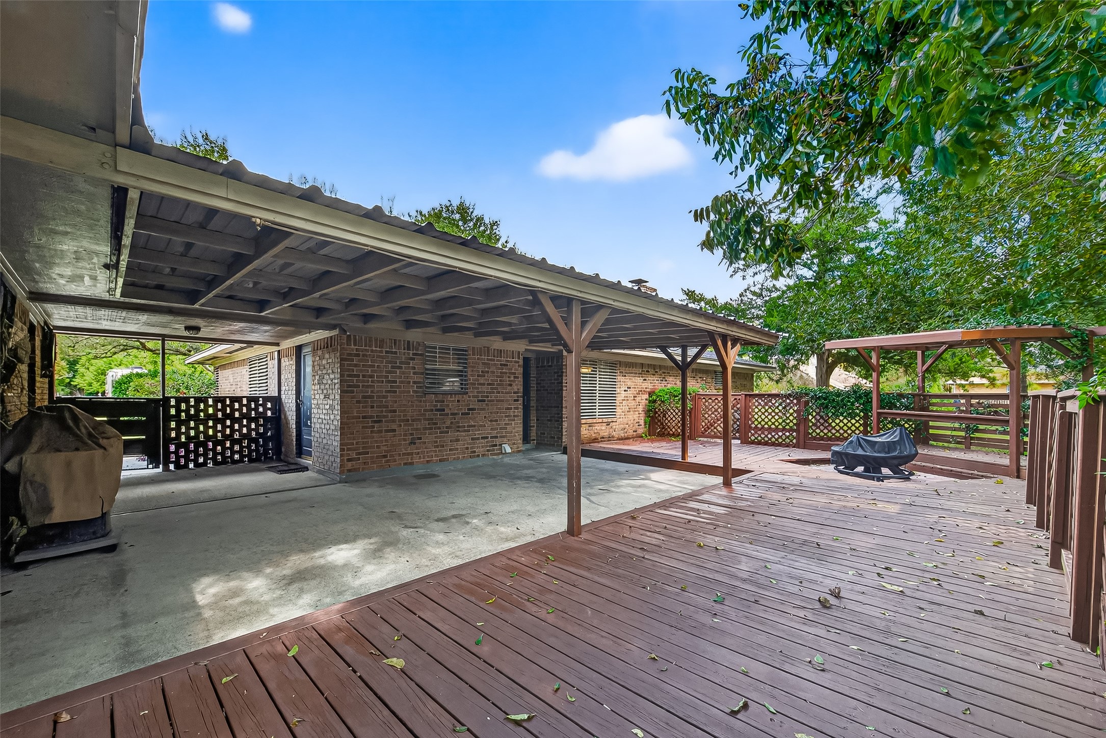 Spacious backyard with a large wooden deck and covered patio area. Ideal for outdoor entertaining and relaxing, surrounded by mature trees for added privacy.