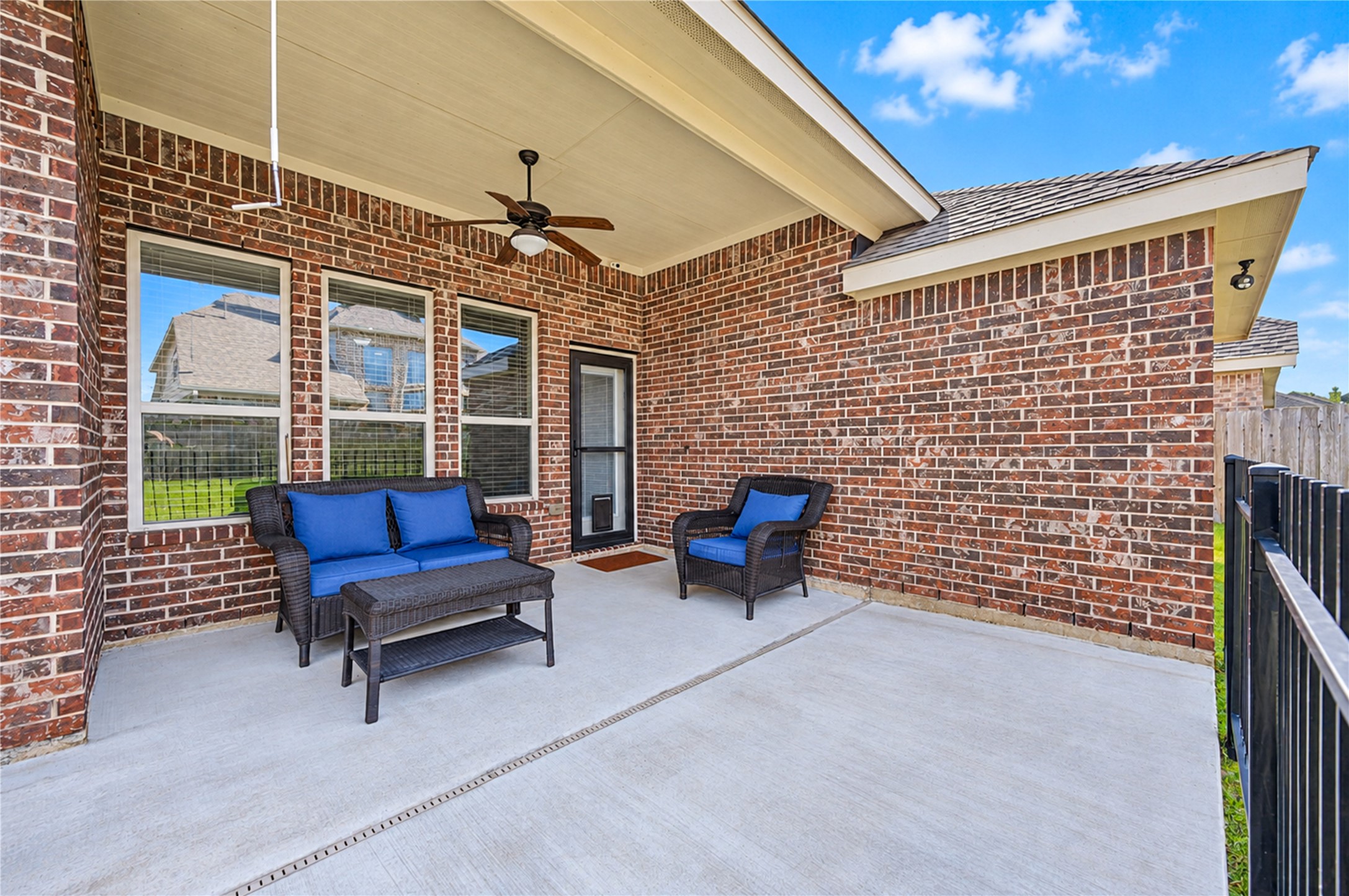 A concrete covered patio with a ceiling fan sits against the home's brick exterior.