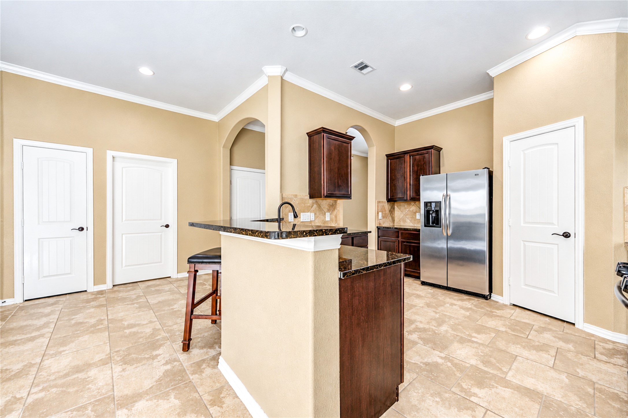The kitchen island with its granite counter sits at the center of a bright, open plan with tile floors throughout.