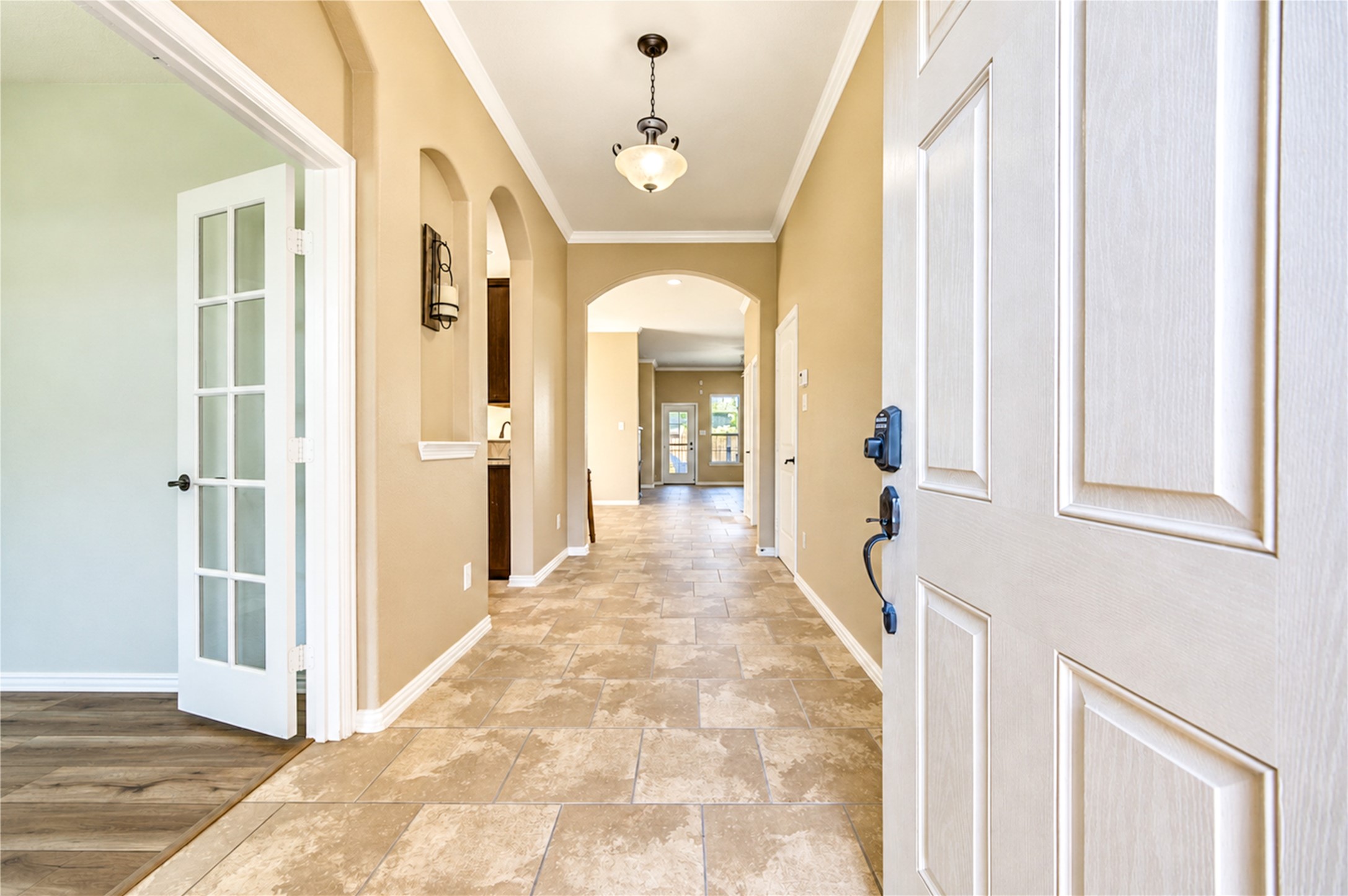 Arched niches and a glass-paneled door at the study line the gallery hall leading to the open living spaces.