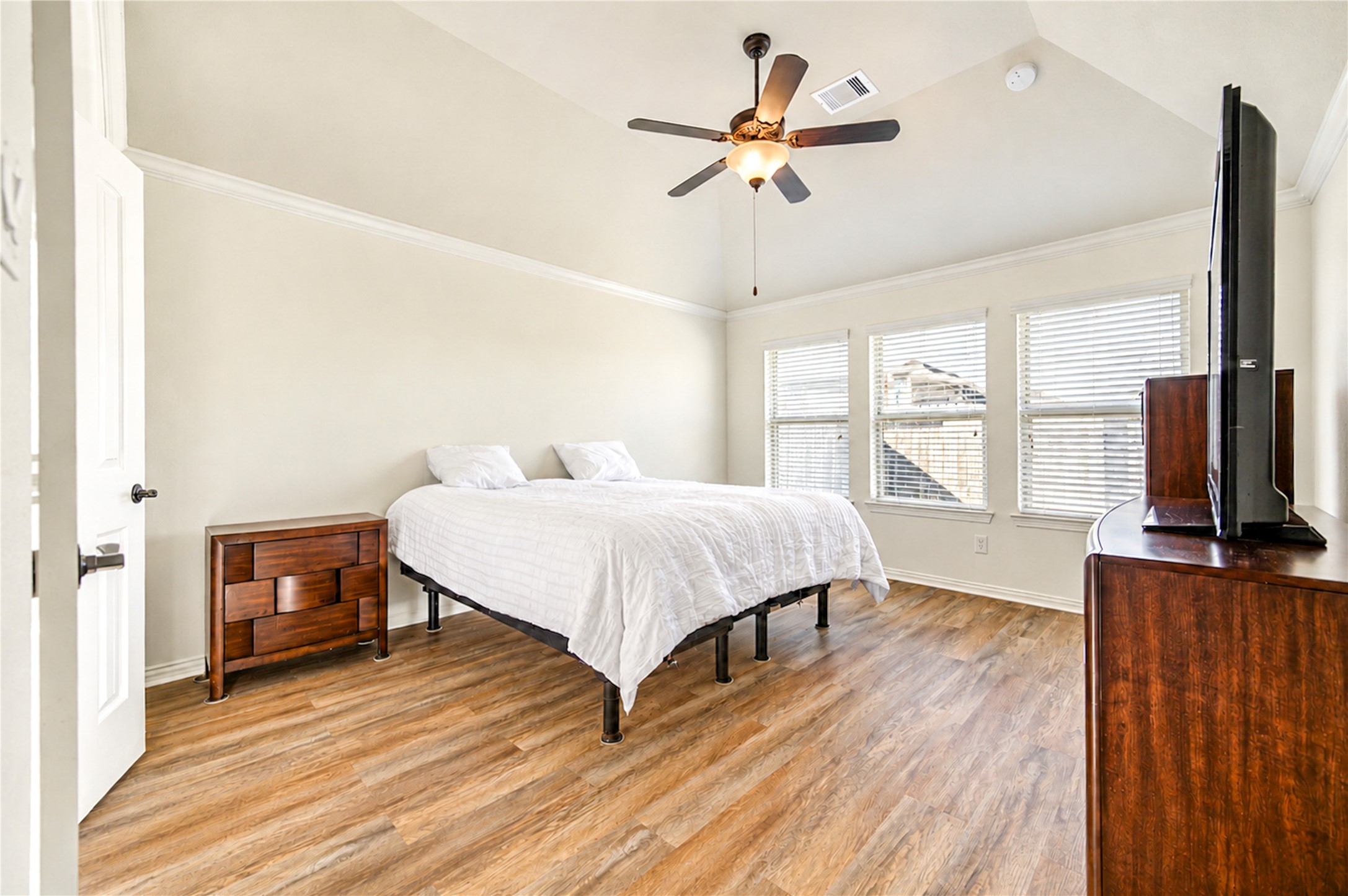 The primary bedroom has a vaulted ceiling, luxury vinyl plank flooring and a bank of windows.
