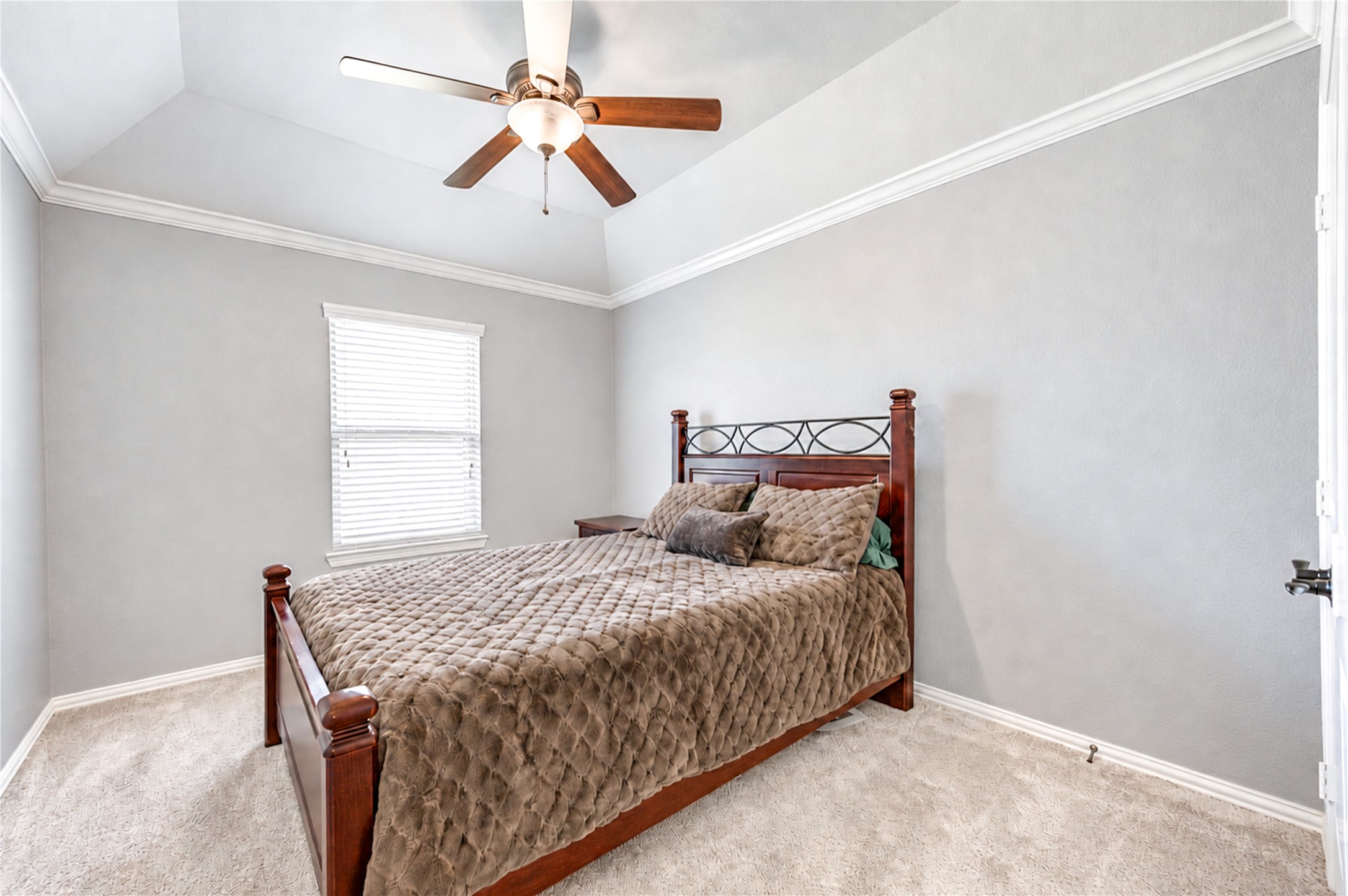 A secondary bedroom with a vaulted ceiling, ceiling fan and soft carpet.
