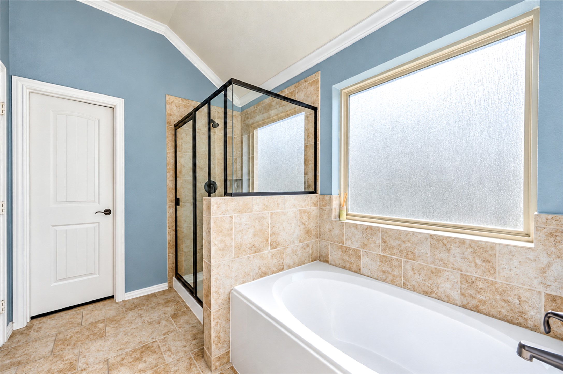 A soaking tub and glass-enclosed shower sit beneath a frosted window in the primary bath.