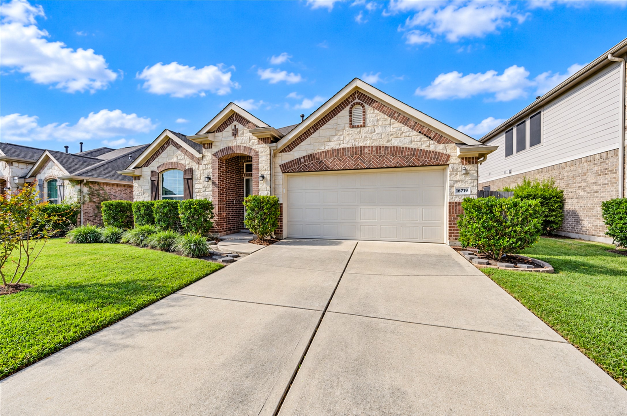 A gabled front elevation of stone and brick with an arched entry and a two-car garage, set behind a manicured lawn.