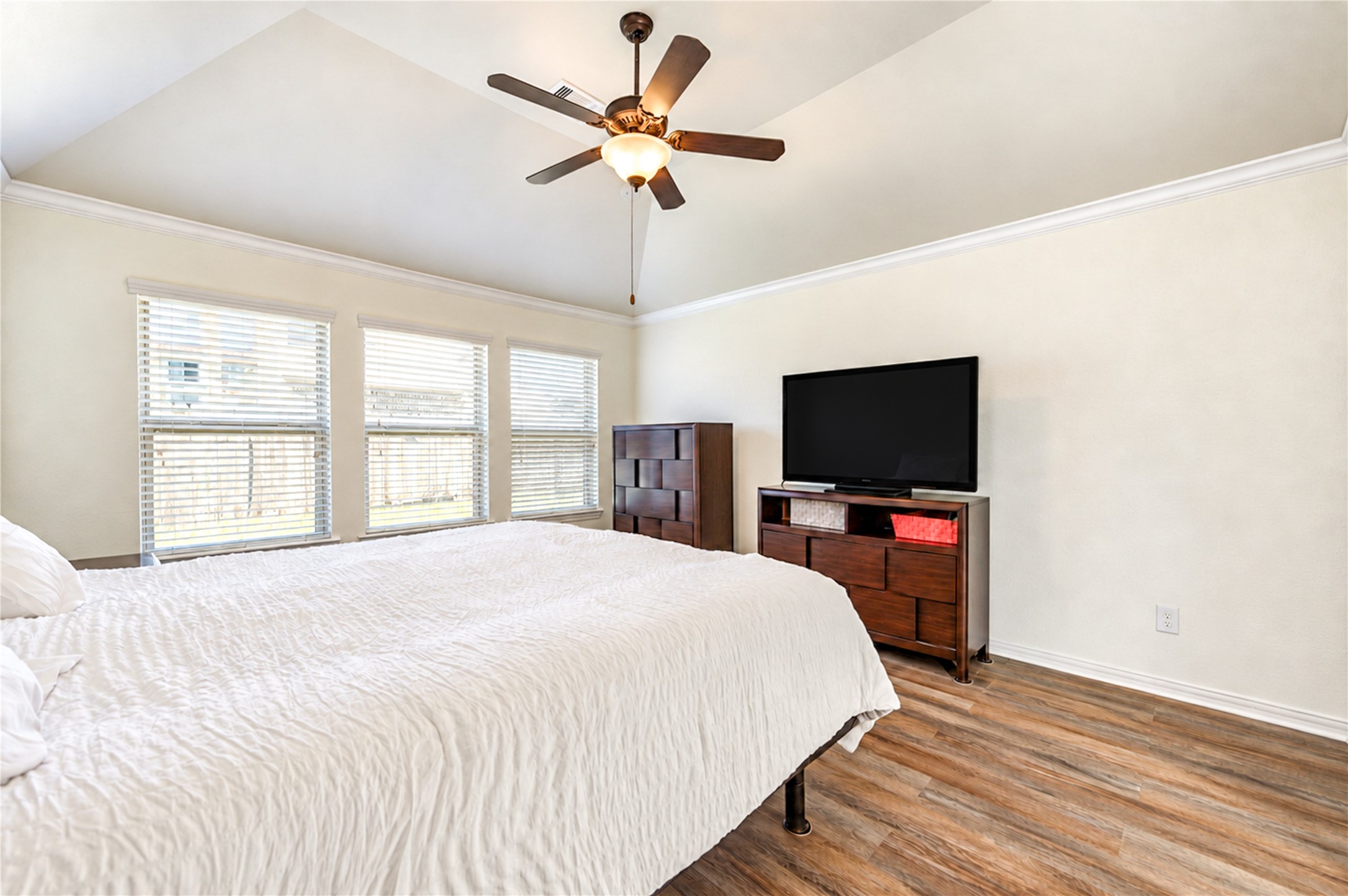 Triple windows fill the primary bedroom with light beneath a high, angled ceiling.