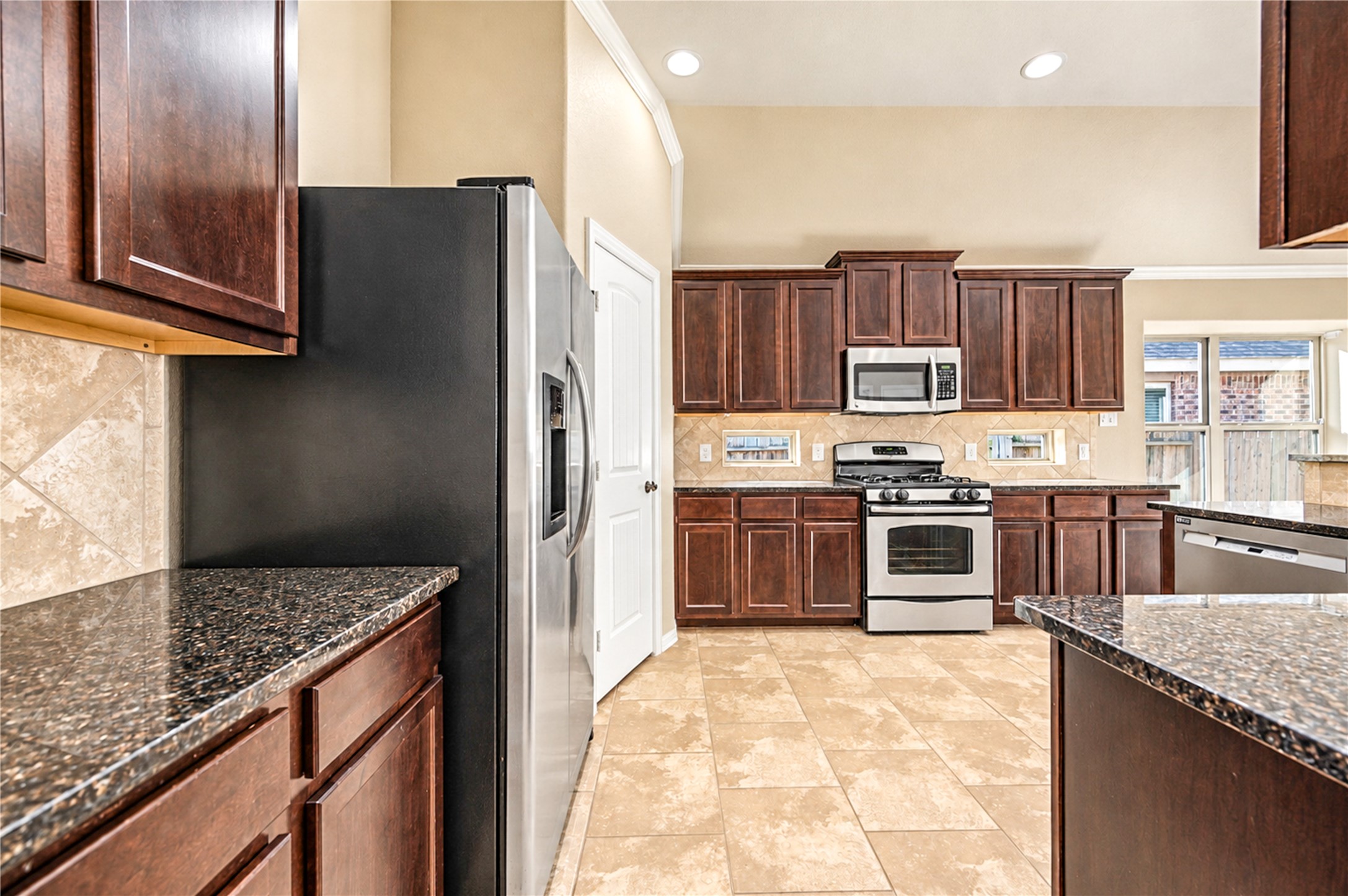 Dark wood cabinetry, granite counters and a gas range define the kitchen, with the pantry just beyond.