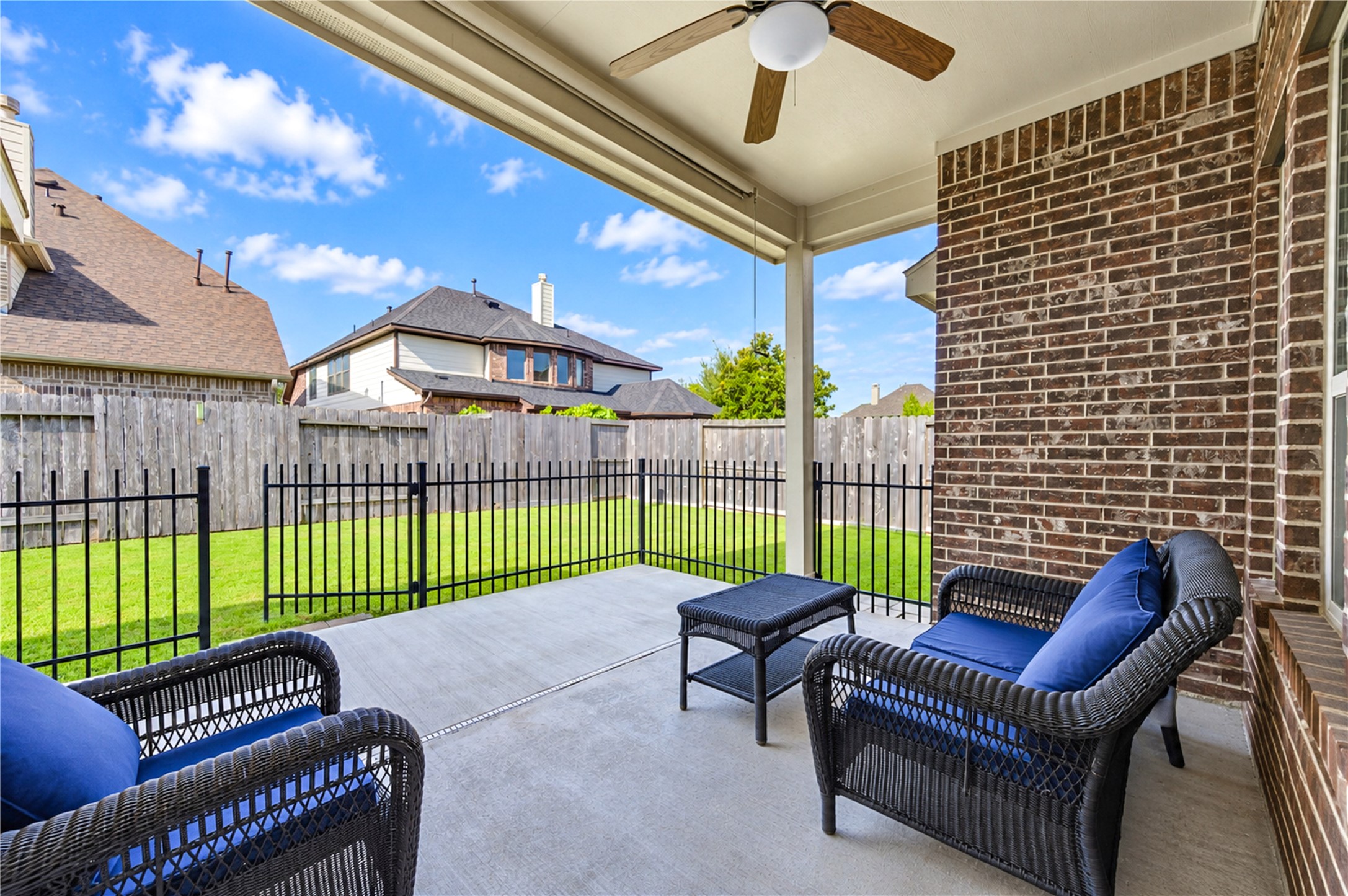 The covered patio extends the living space outdoors, with brick walls and a wrought-iron fence enclosing the yard.