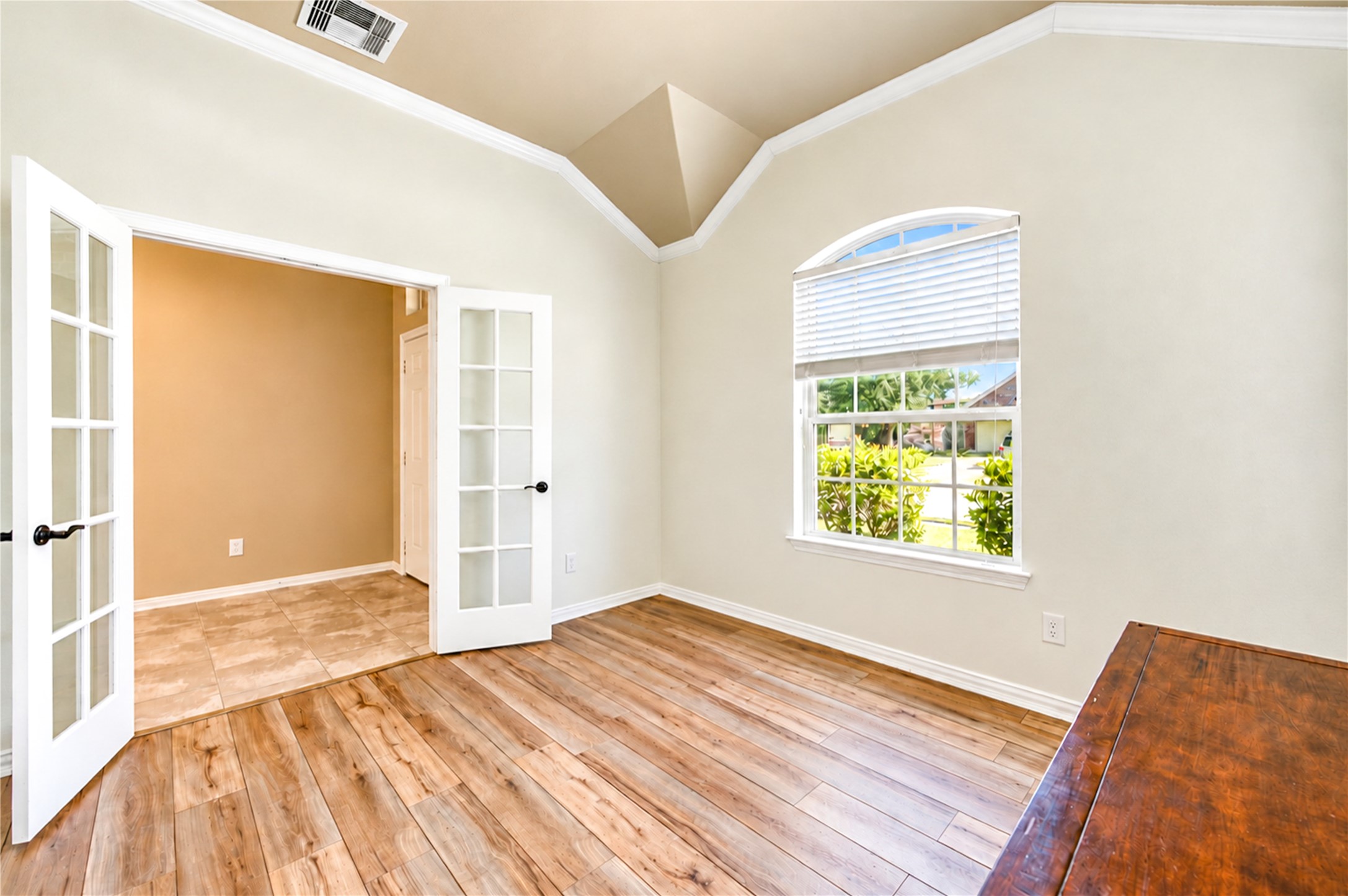 French doors open to the home office, where luxury vinyl plank flooring and an arched window create a quiet workspace.