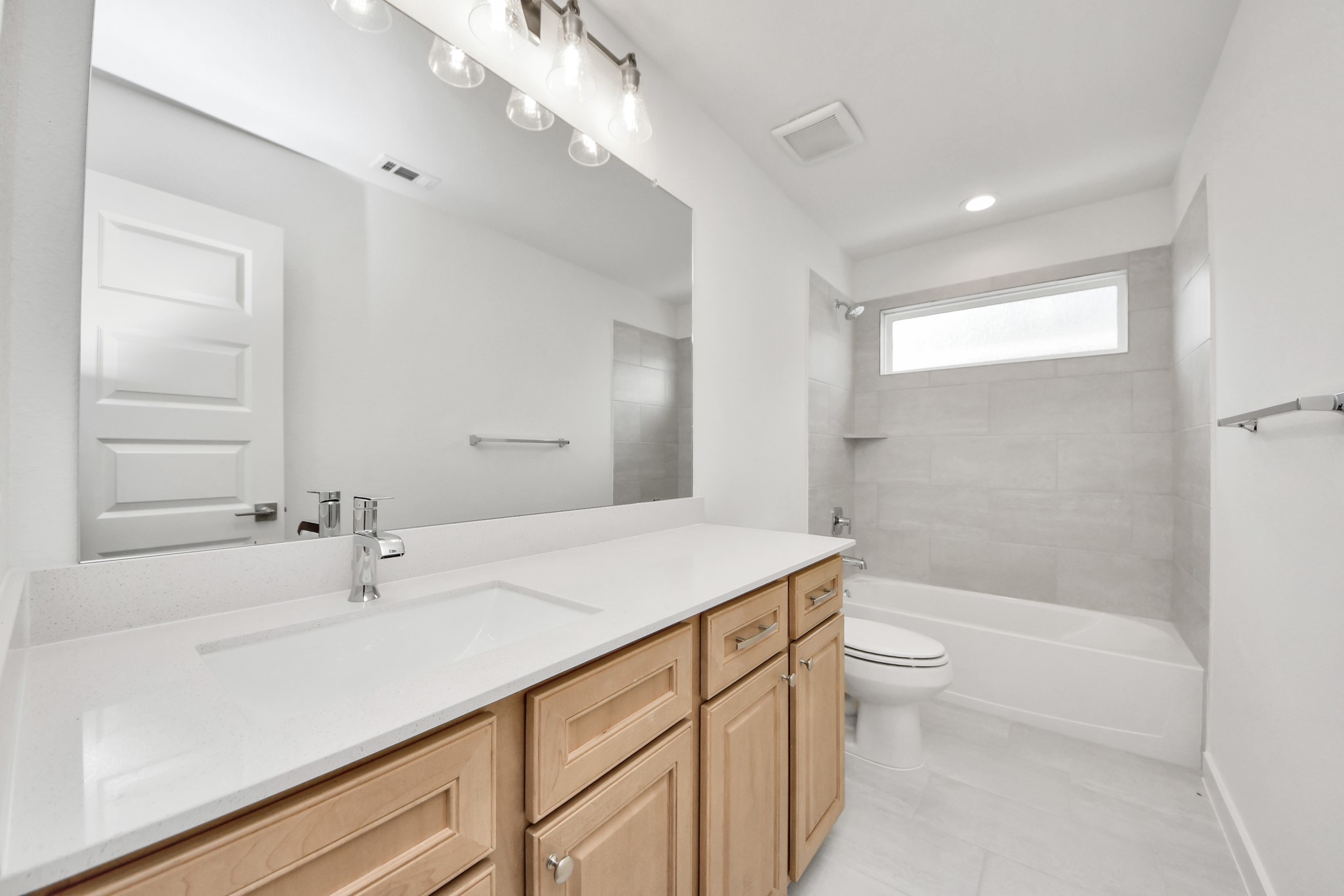 Secondary bath features tile flooring, bath/shower combo with tile surround, light stained wood cabinets, beautiful light countertop. Sample photo of completed home with similar floor plan. Actual colors and selections may vary.