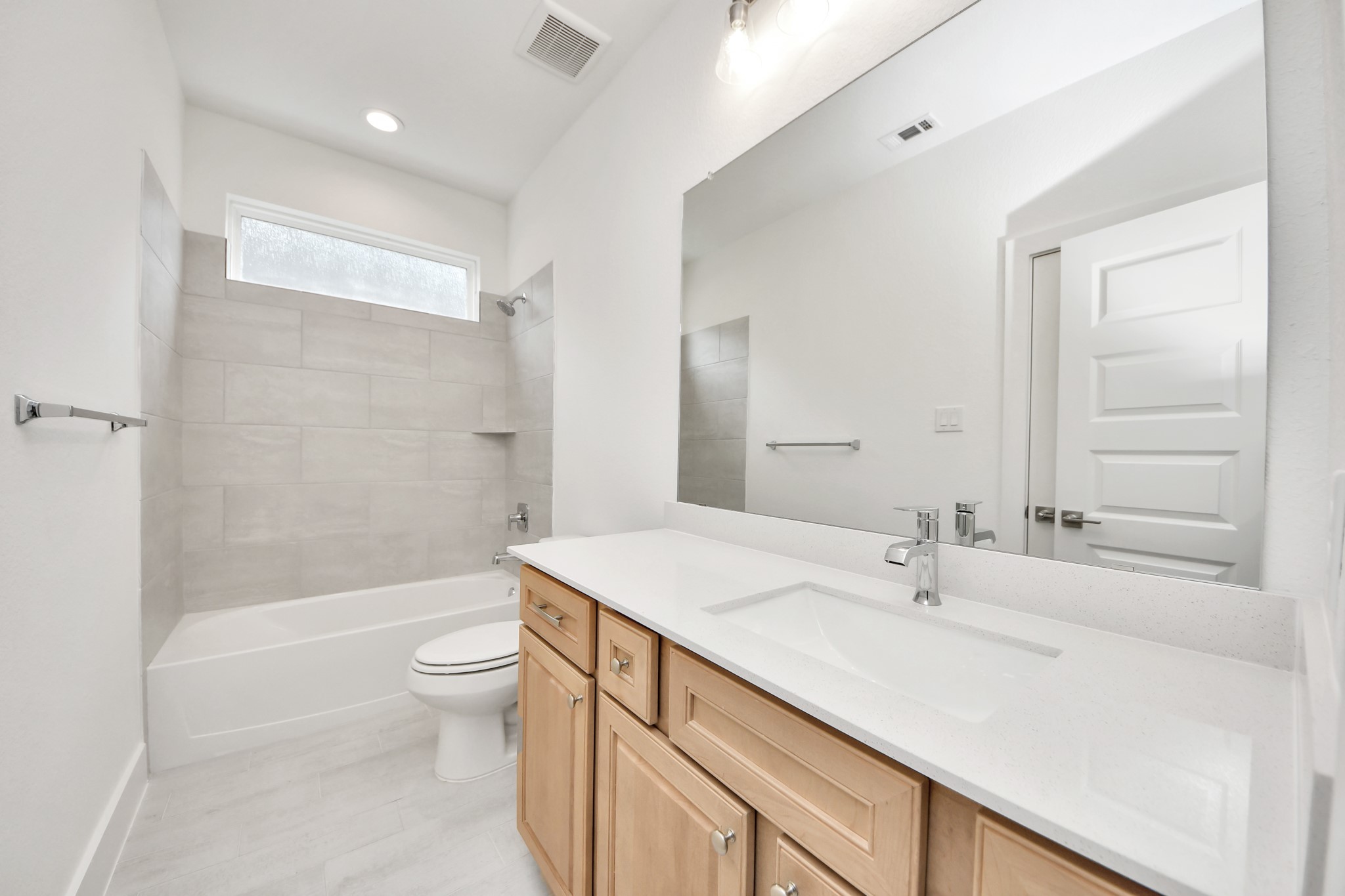 Secondary bath features tile flooring, bath/shower combo with tile surround, light stained wood cabinets, beautiful light countertop. Sample photo of completed home with similar floor plan. Actual colors and selections may vary.