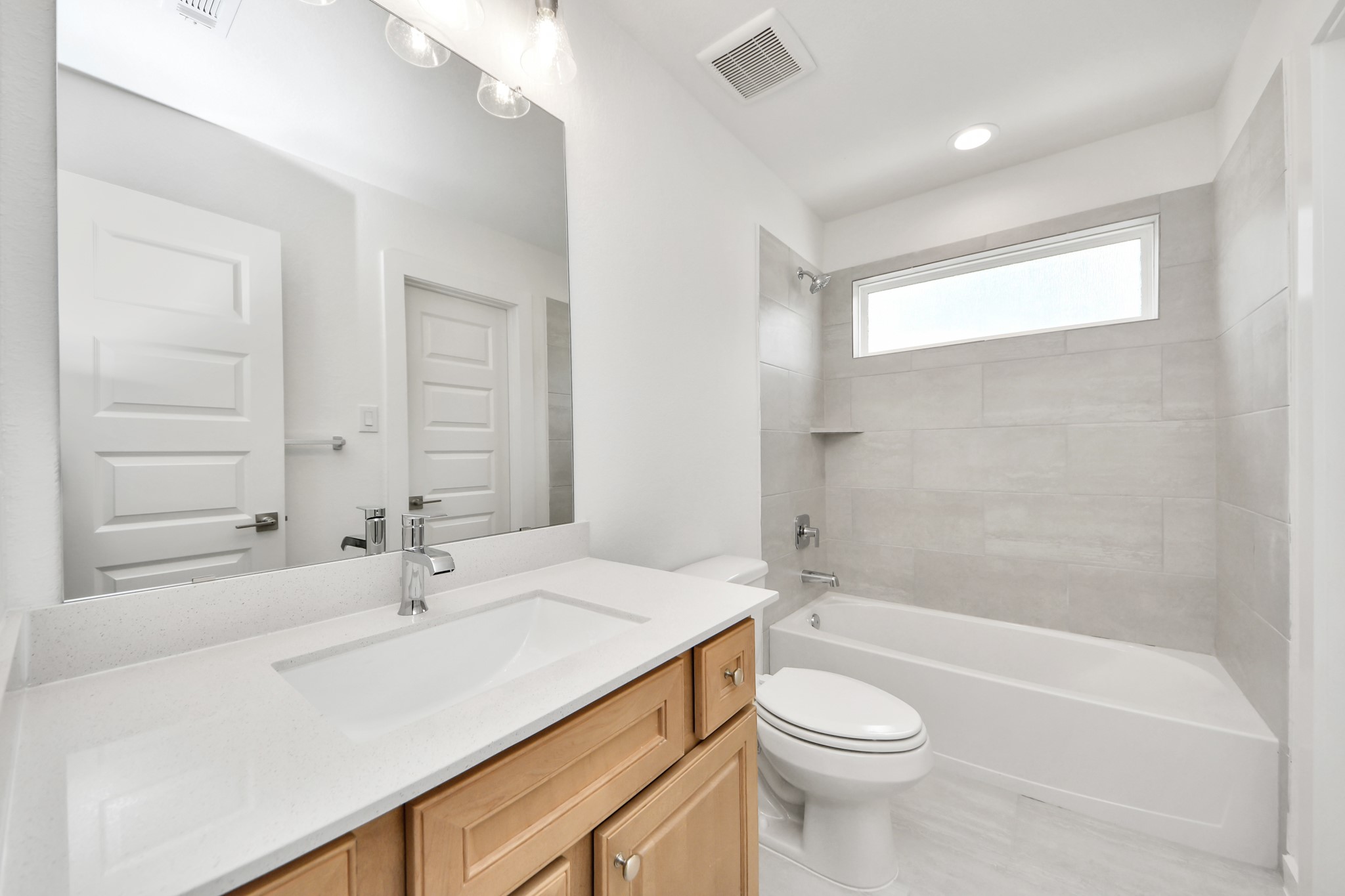 Secondary bath features tile flooring, bath/shower combo with tile surround, light stained wood cabinets, beautiful light countertop. Sample photo of completed home with similar floor plan. Actual colors and selections may vary.