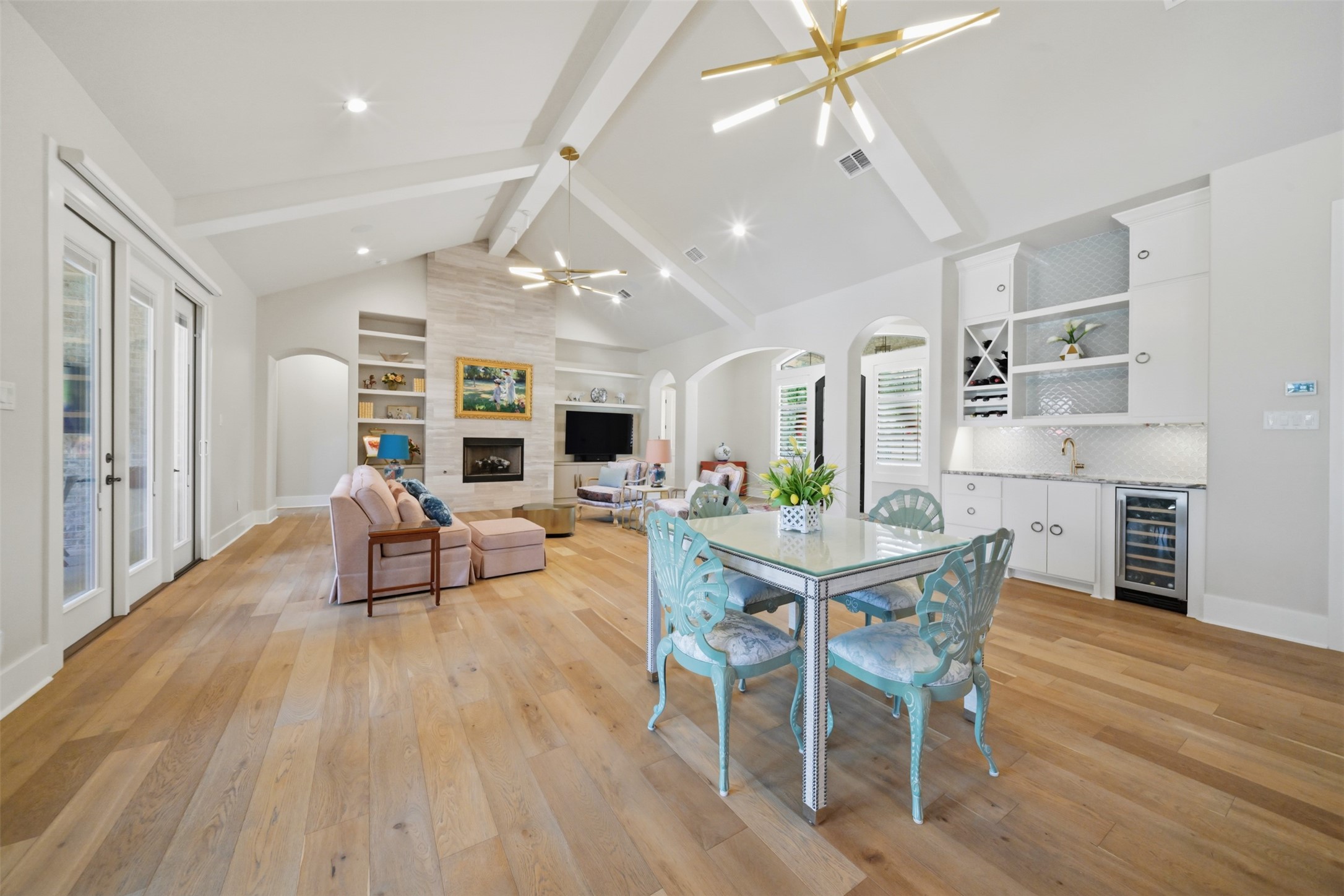 Oversized open dining area with room for a large dining table, conveniently positioned beside the wet bar, with custom built-ins, beverage refrigerator, wide-plank wood flooring and soaring beamed ceiling.