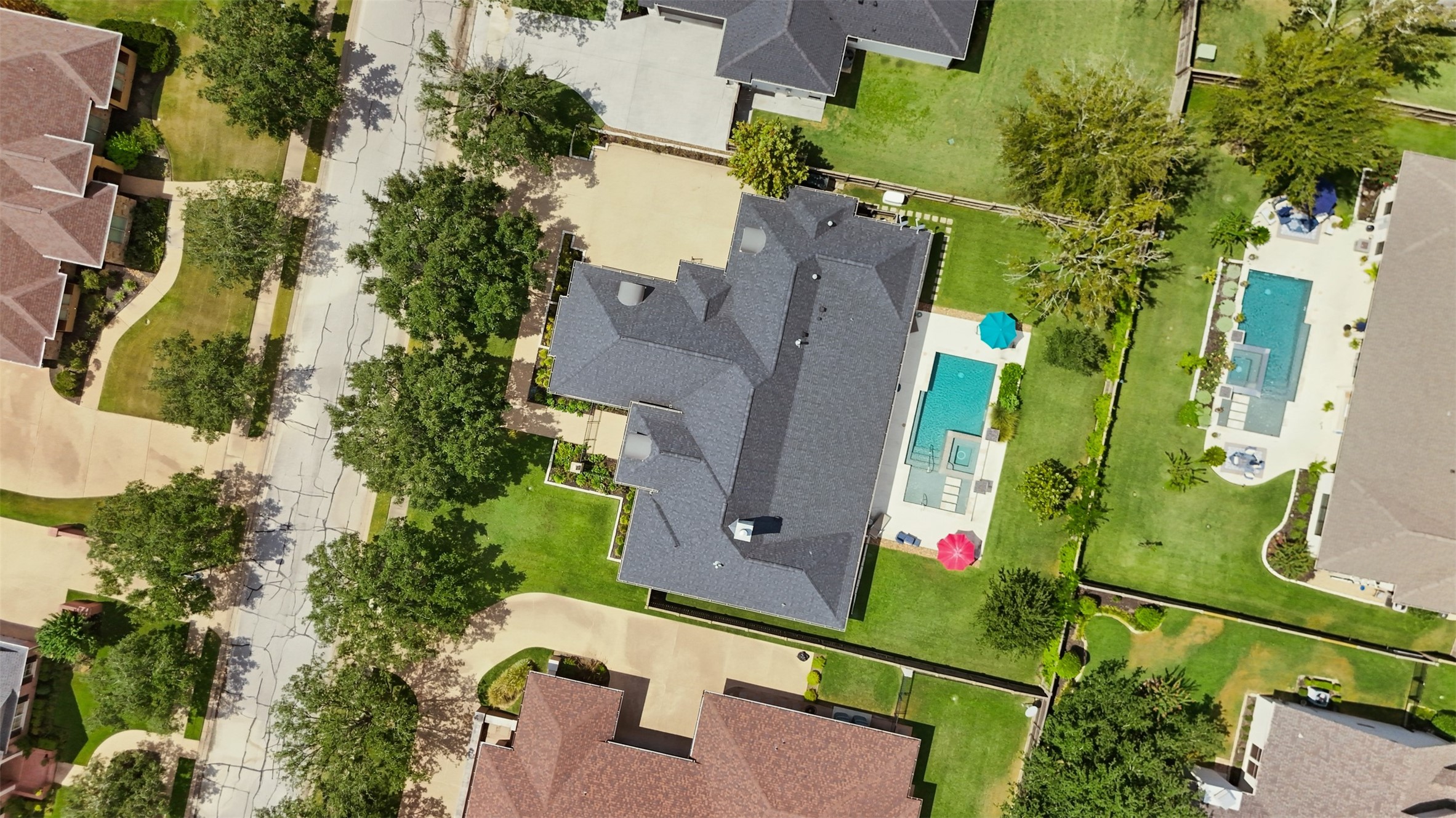 Aerial view of the entire property highlighting the homes footprint, generous lot, driveway, sidewalks, pool, and surrounding green space.