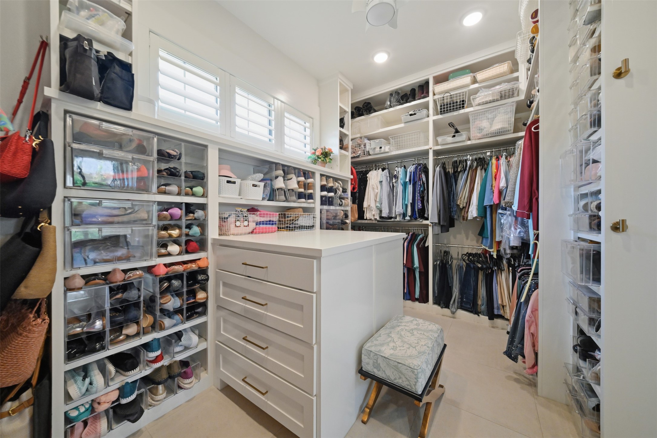 Roomy primary closet with custom built-ins, abundant hanging and shoe storage, a center storage island, and direct access to both the primary bathroom and laundry room.