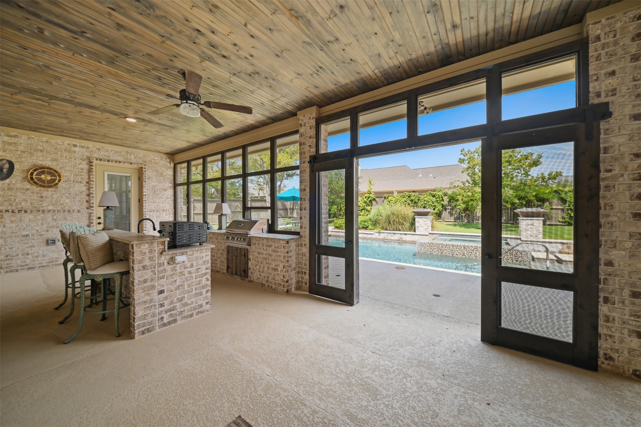 Another view of the expansive screened-in porch, highlighting the outdoor kitchen, stained wood ceiling and direct access to the pool.