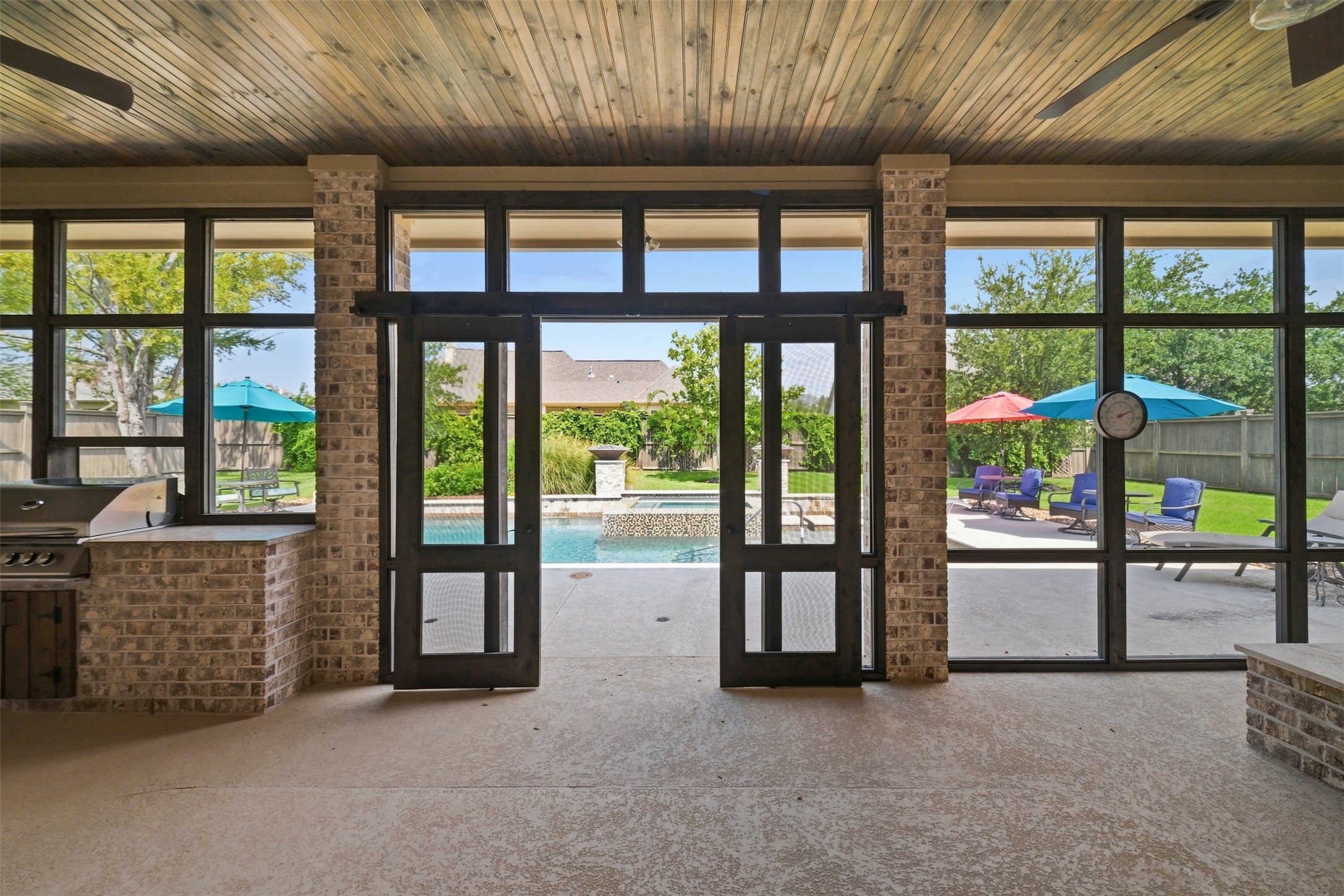 Expansive screened-in porch with a stained wood ceiling and ceiling fans opens directly to the pool, with the outdoor kitchen and fire pit just steps away.